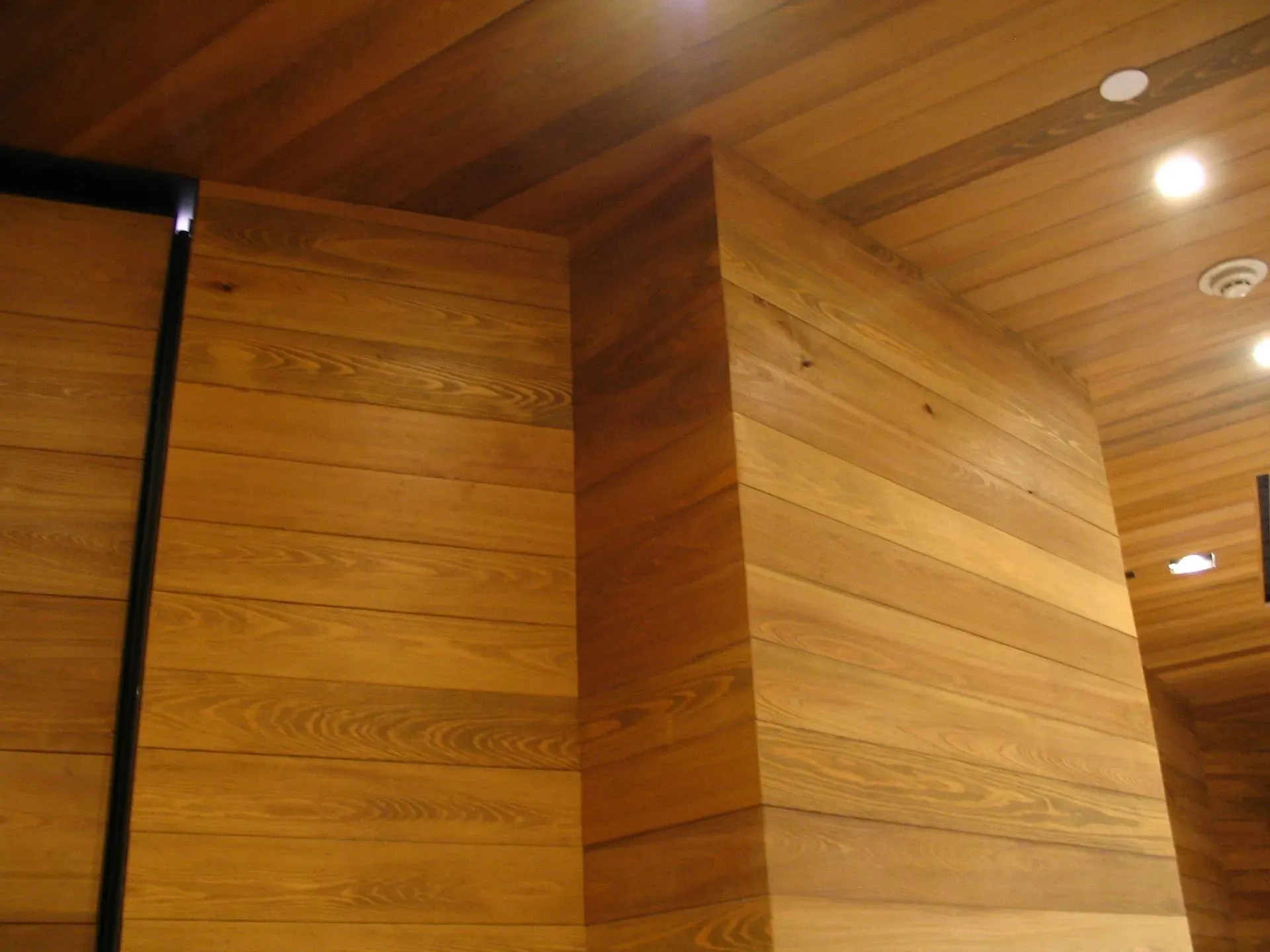 Wood-paneled interior corner with recessed ceiling lights and wood ceiling beams