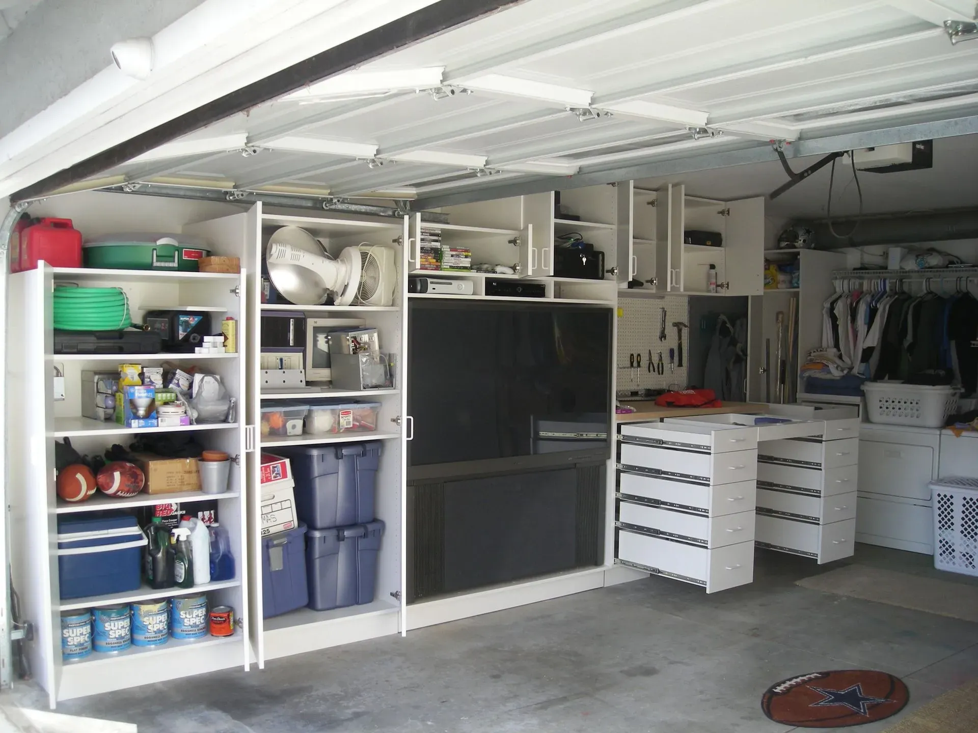 Garage workshop with shelves of tools, storage bins, and a workbench under fluorescent lights