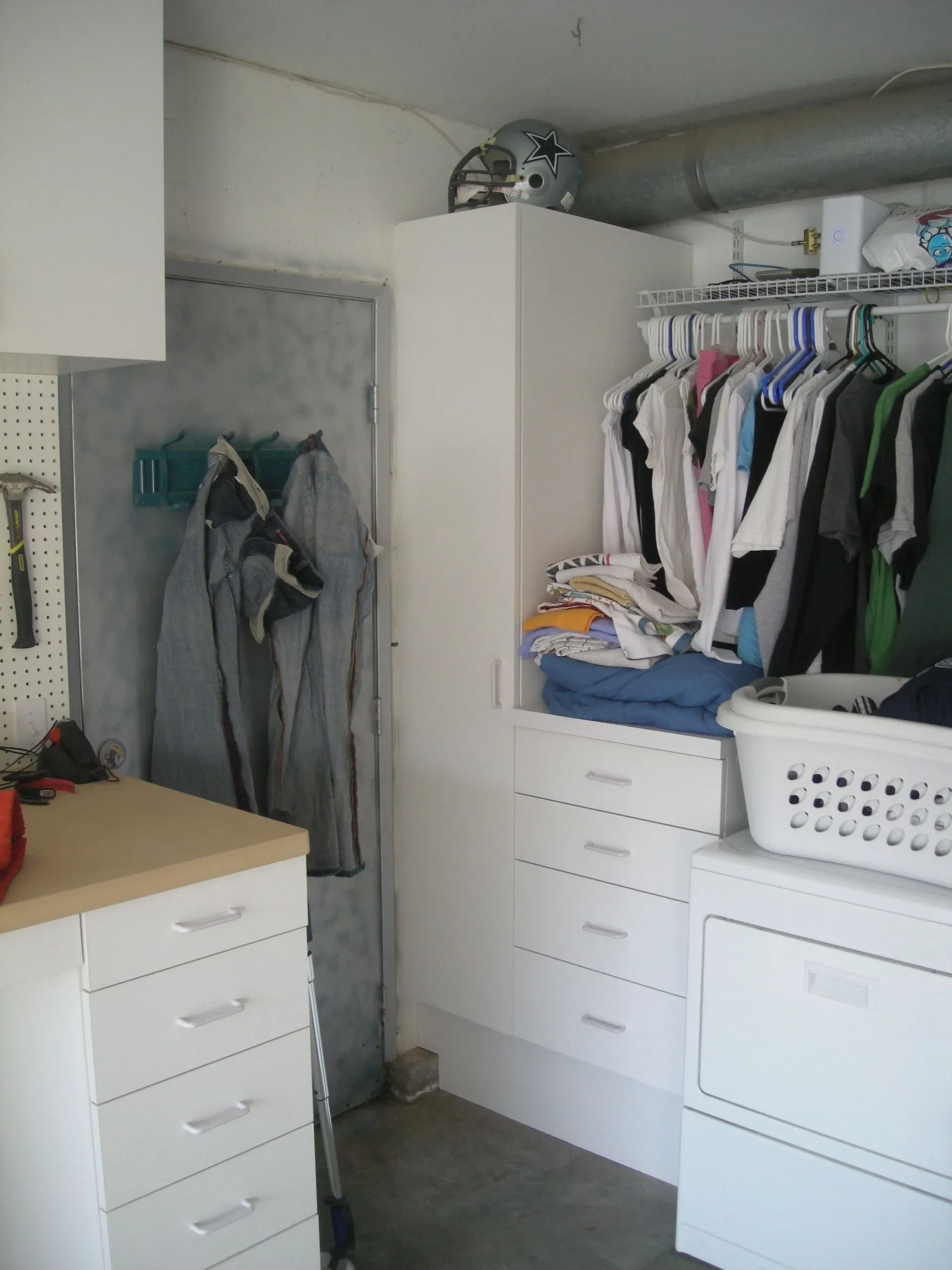 Closet laundry area with hanging clothes, drawers, and an ironing board in a small room