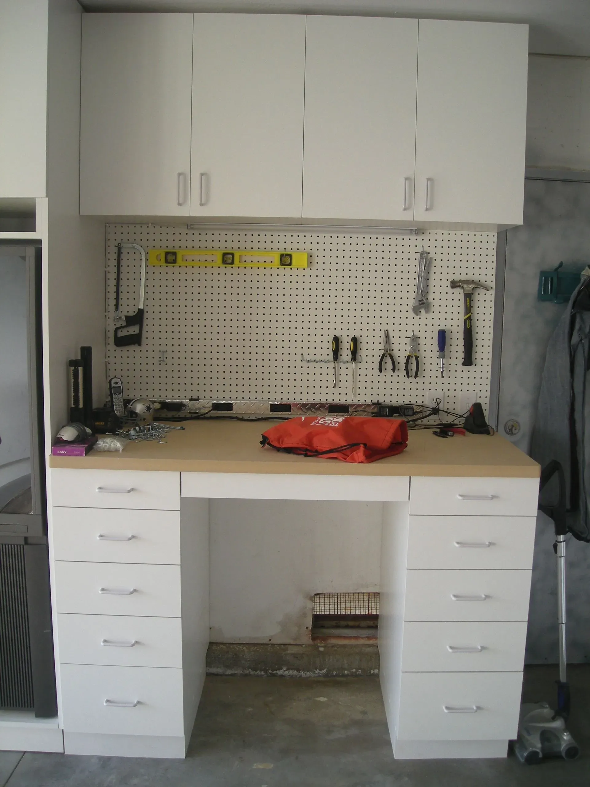 White garage workbench with cabinets, pegboard tools, and red cloth on countertop