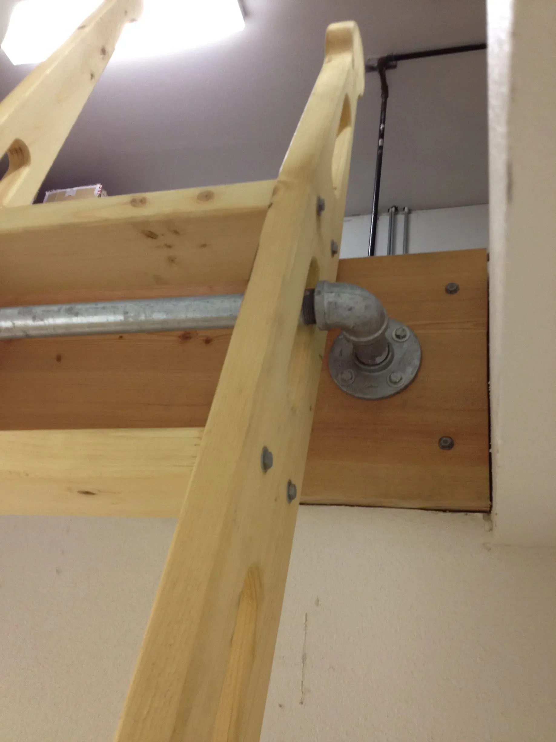 Wooden loft ladder hinged to a ceiling opening with a metal bracket and support bar.