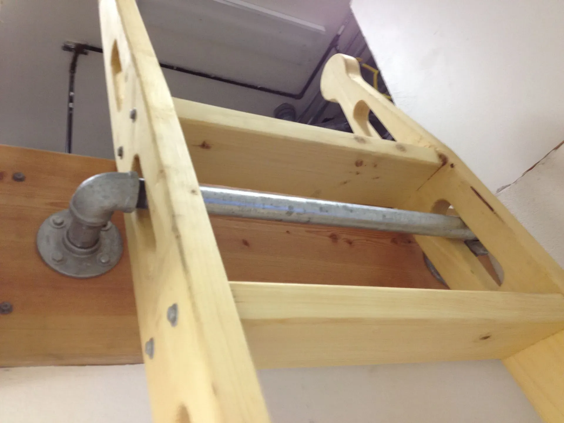 Wooden attic ladder with metal rungs folded against a ceiling hatch, viewed from below