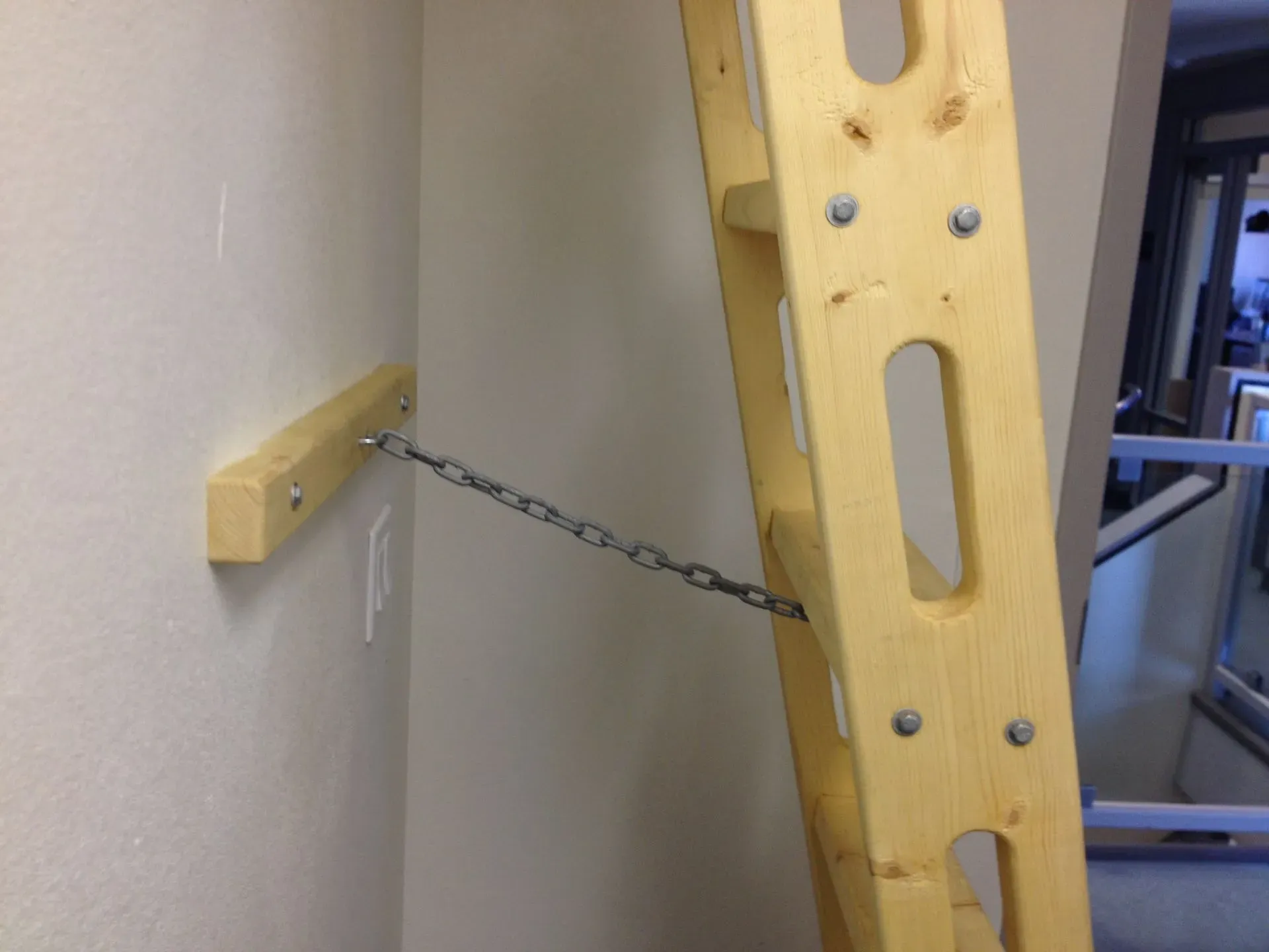 Yellow ladder braced against a wall with a chain anchored to a wooden block for support