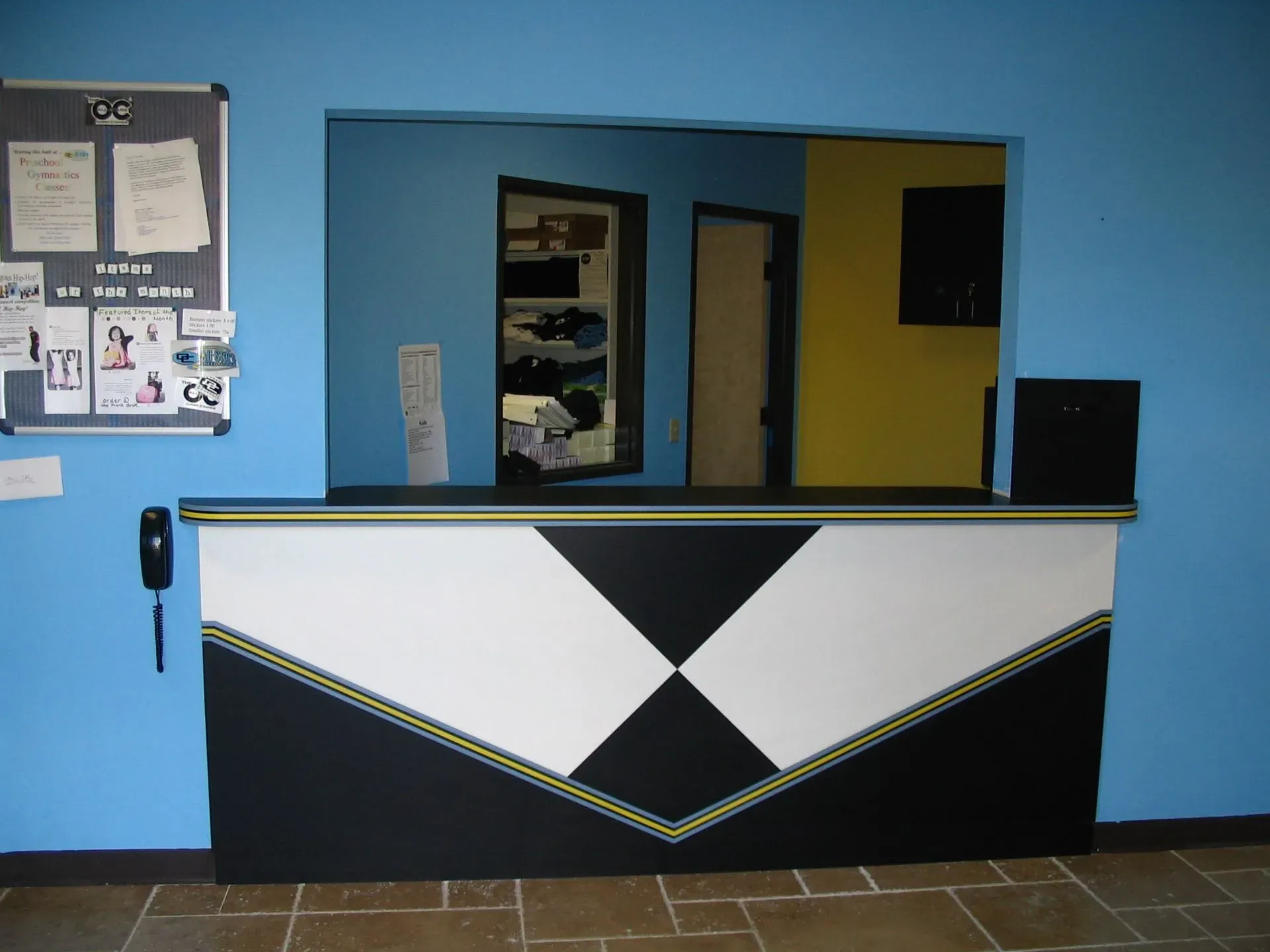 Blue lobby with a black-and-white reception desk and a window opening to an interior office.