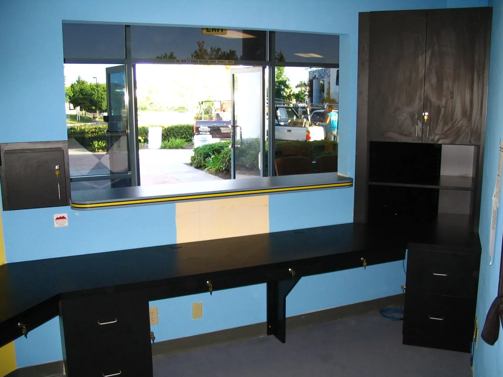 Blue office desk with mirror, black shelves, and wood paneling in a small room