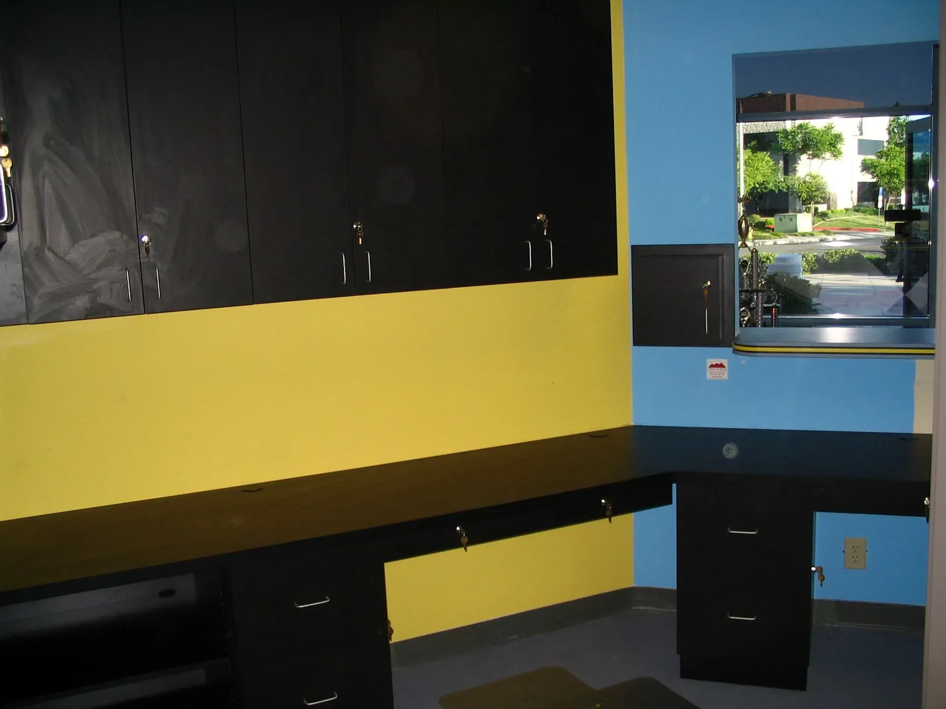 Small room with blackboard wall, yellow and blue walls, desk, and a window to greenery outside.