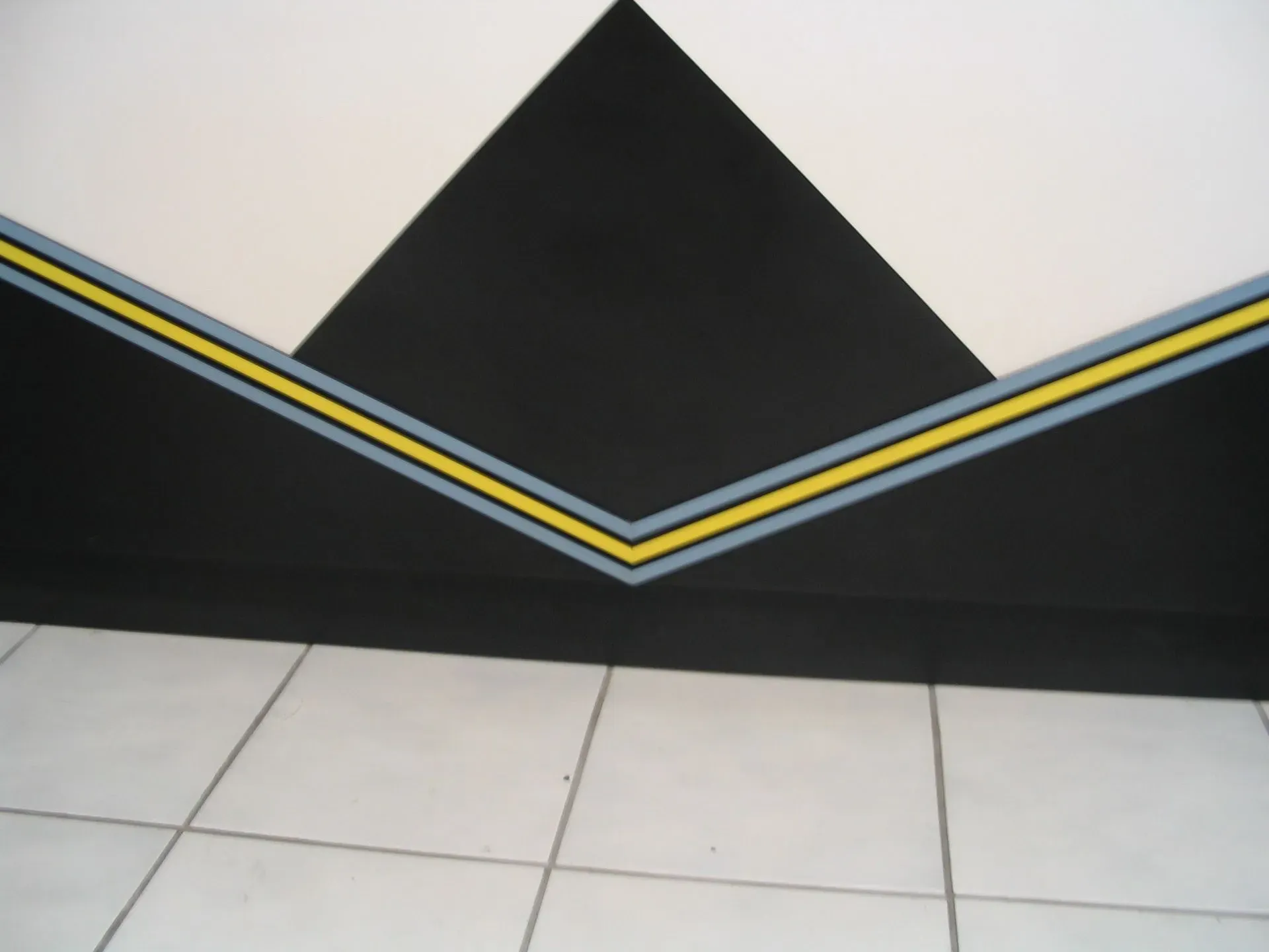 Black and white wall with diagonal yellow and blue stripes above light gray tiled floor