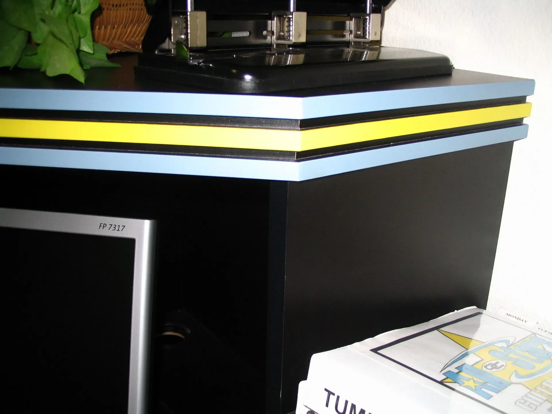 Black cabinet with stacked blue, yellow, and white shelves; printer on top and papers beside it