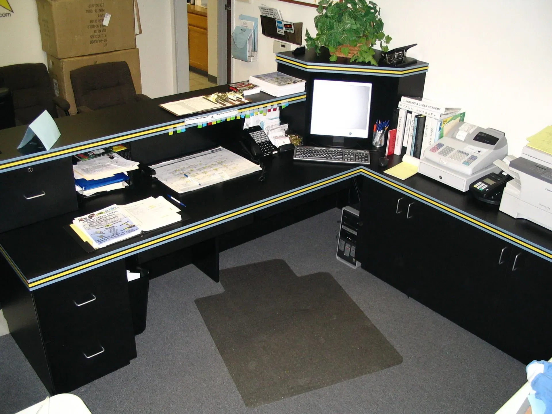 Reception desk in an office, with papers, a phone, computer monitor, and chair behind it.