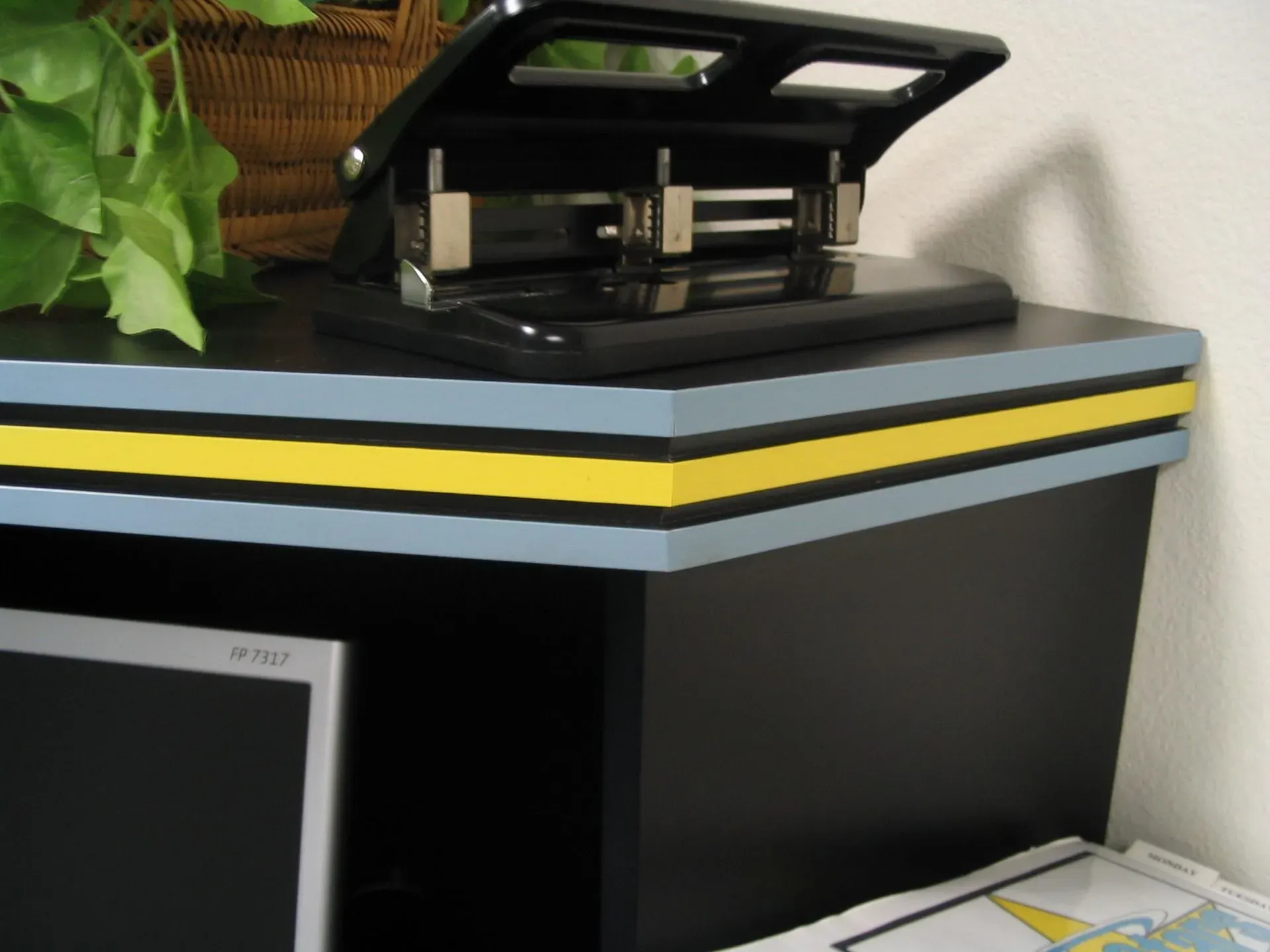 Black printer on a table with a raised lid, next to a potted plant and striped edge trim