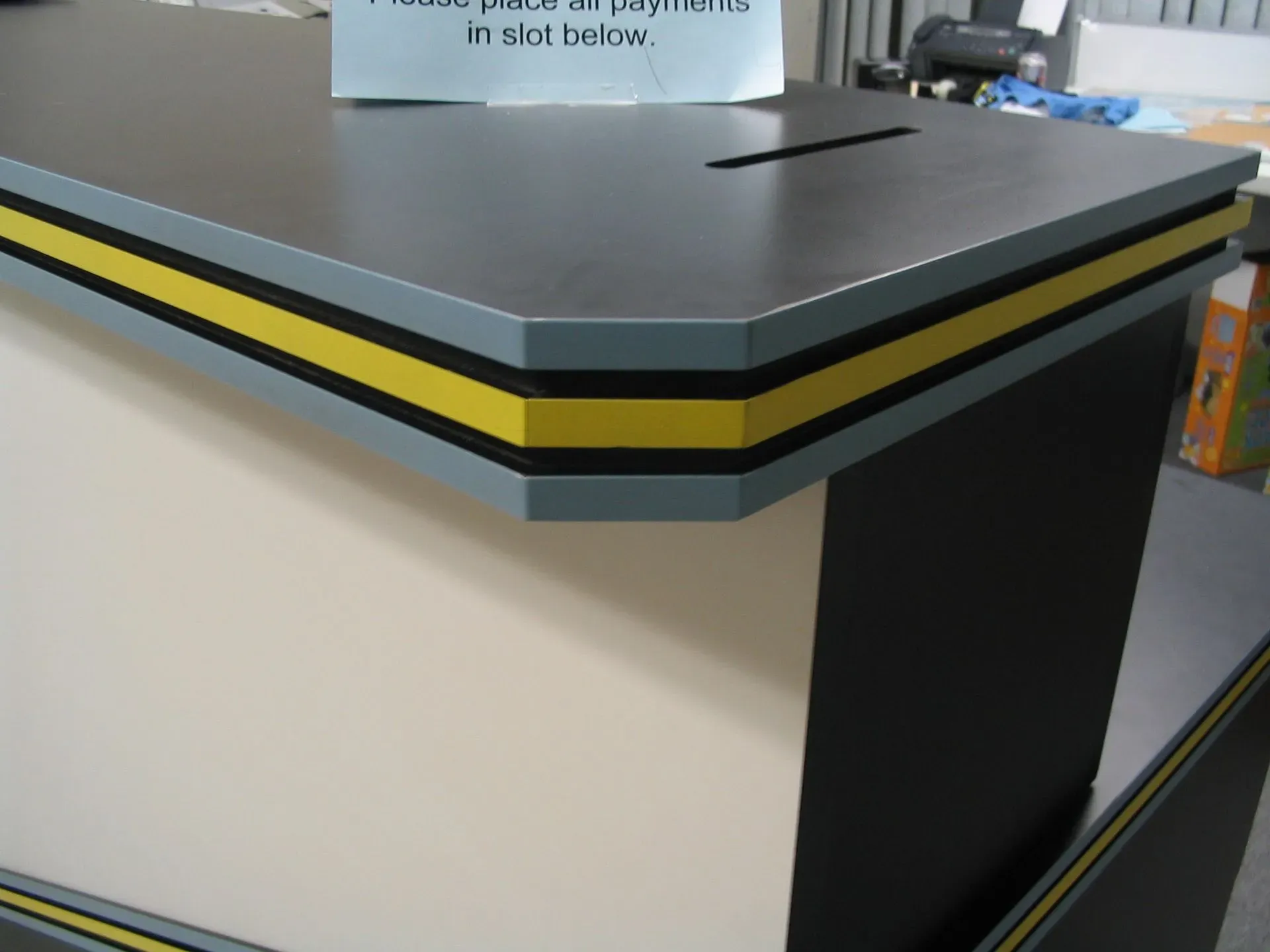 Black display counter with layered gray, yellow, and black trim in a store or museum setting