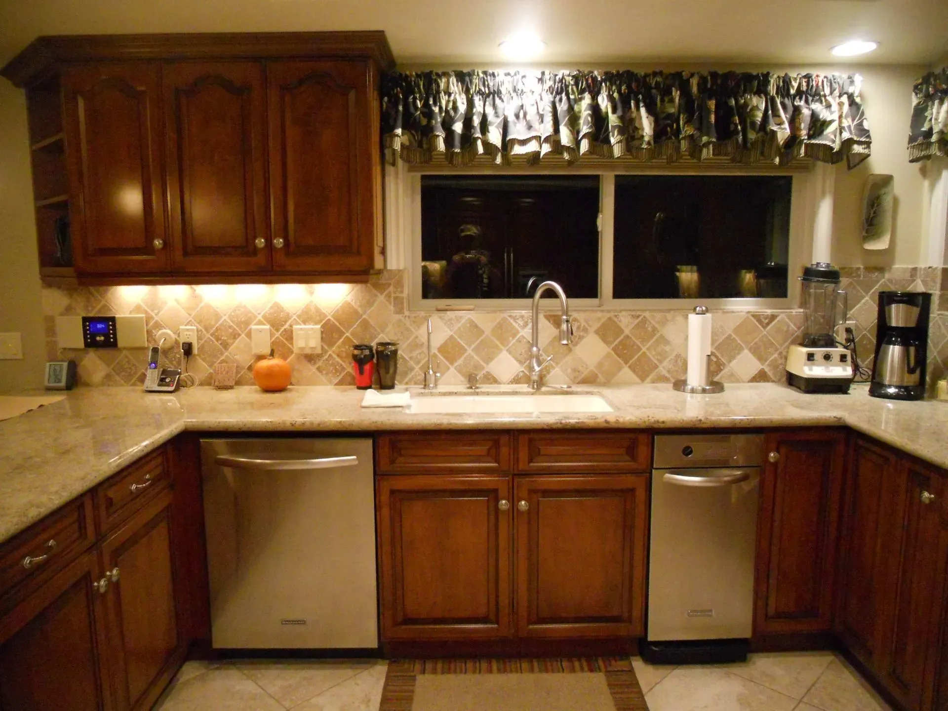 Wooden kitchen with granite counters, stainless appliances, and a window over the sink with floral valance.