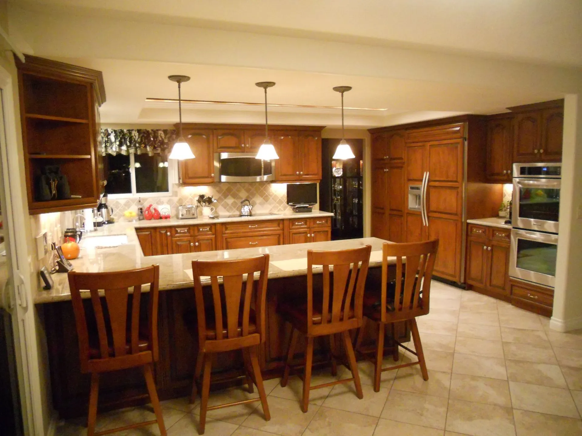 Spacious kitchen with wood cabinets, island stools, and tiled floor under warm pendant lights