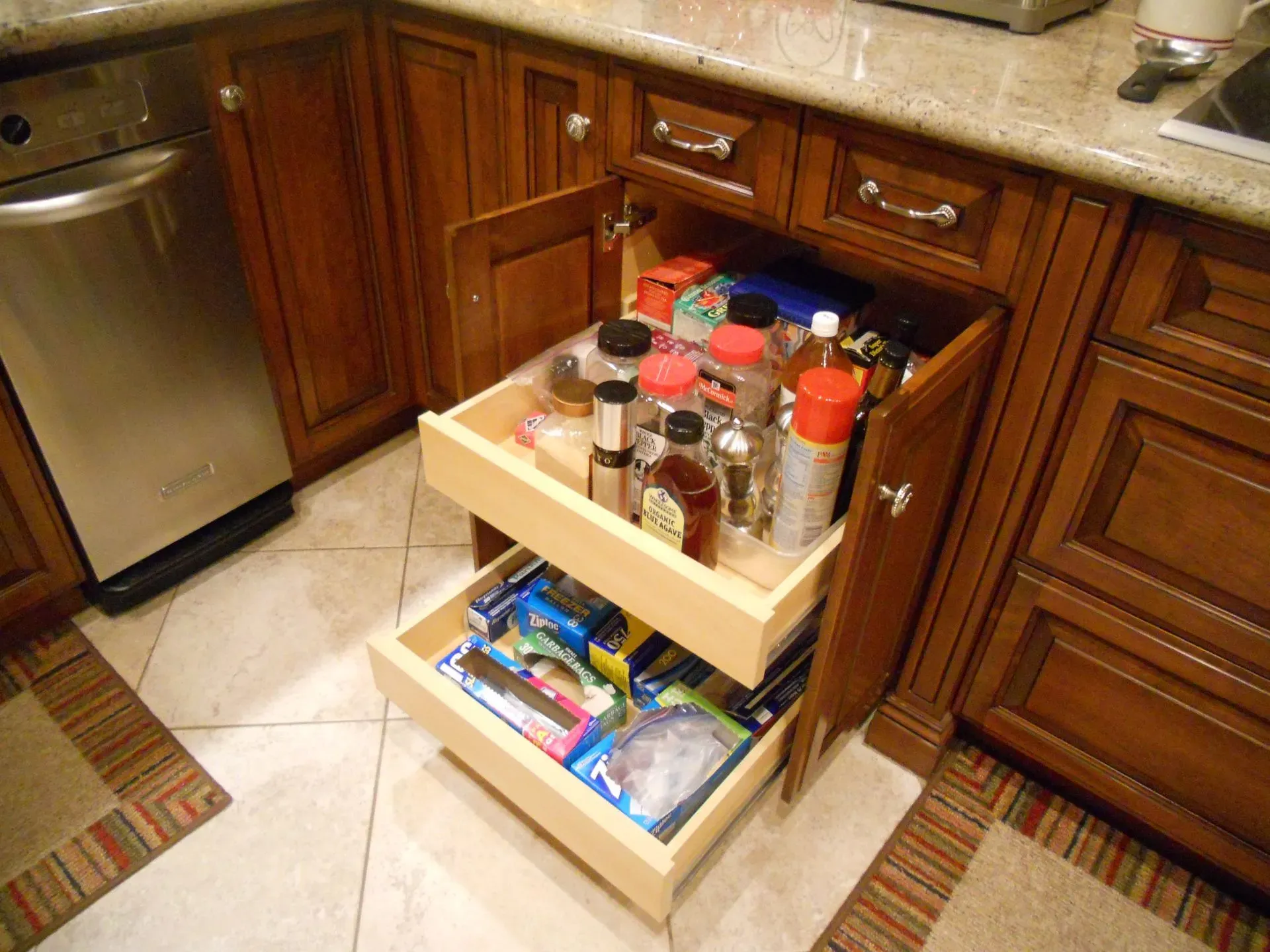 Open kitchen cabinet with pull-out shelves holding spices and packaged food next to a dishwasher.