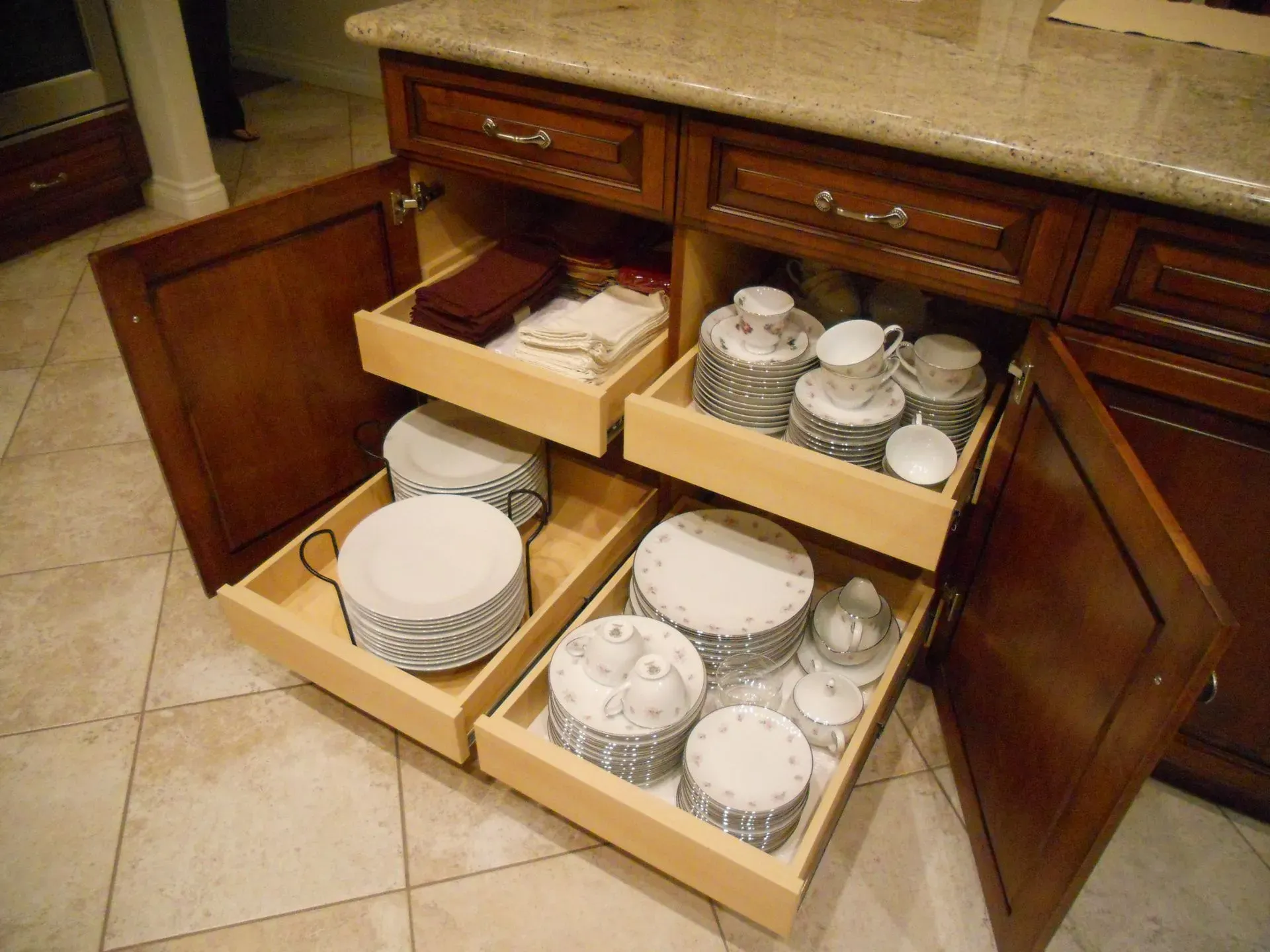Open kitchen cabinet with pull-out drawers holding stacked plates, bowls, and cups.