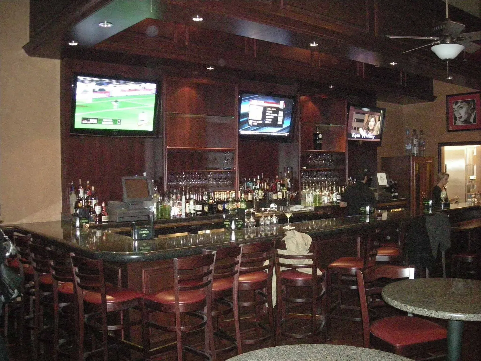 Dim sports bar interior with wooden tables, stools, and multiple TV screens above the counter.