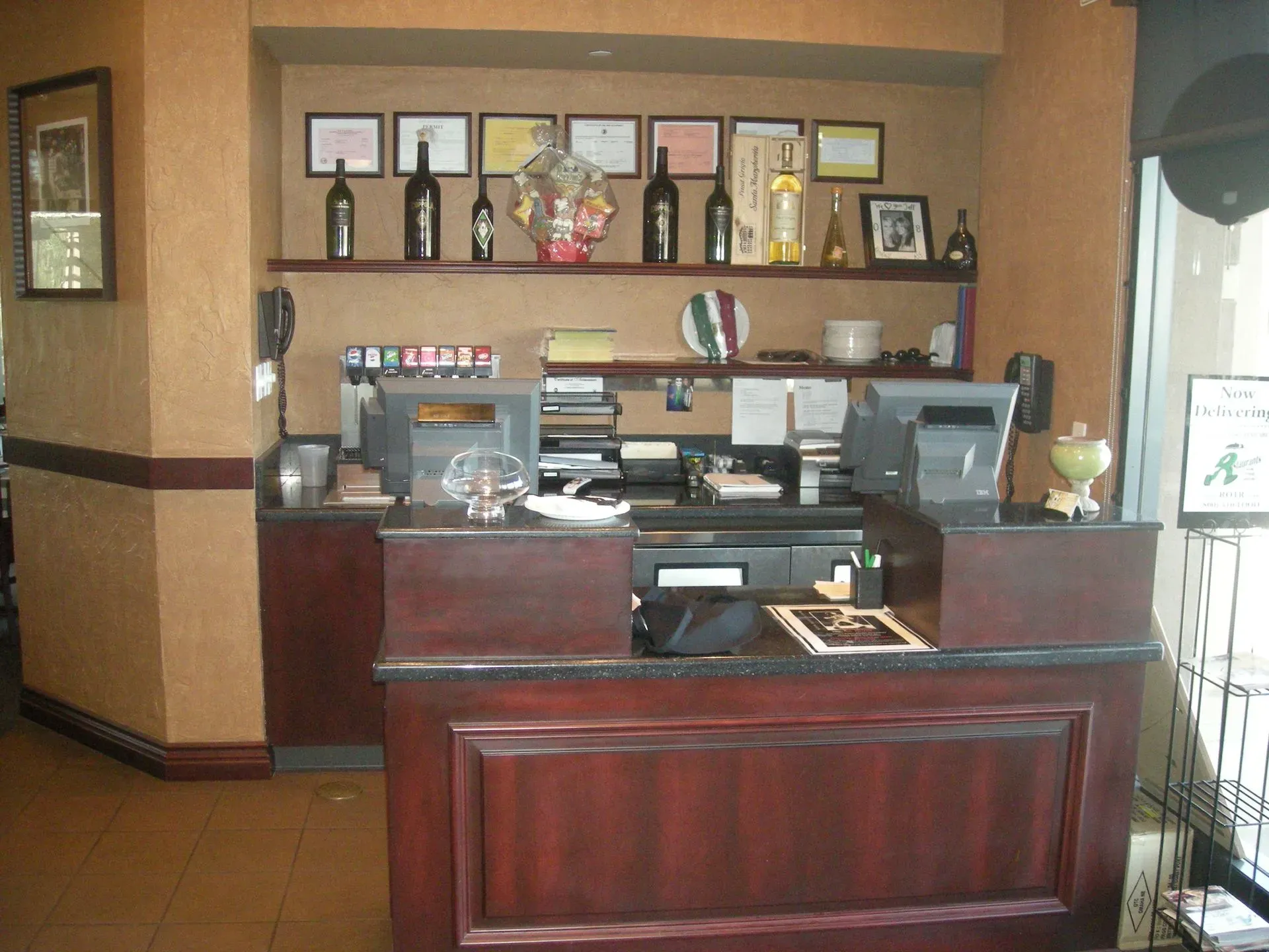 Reception desk in a lobby with framed awards, bottles, and office equipment on shelves behind it