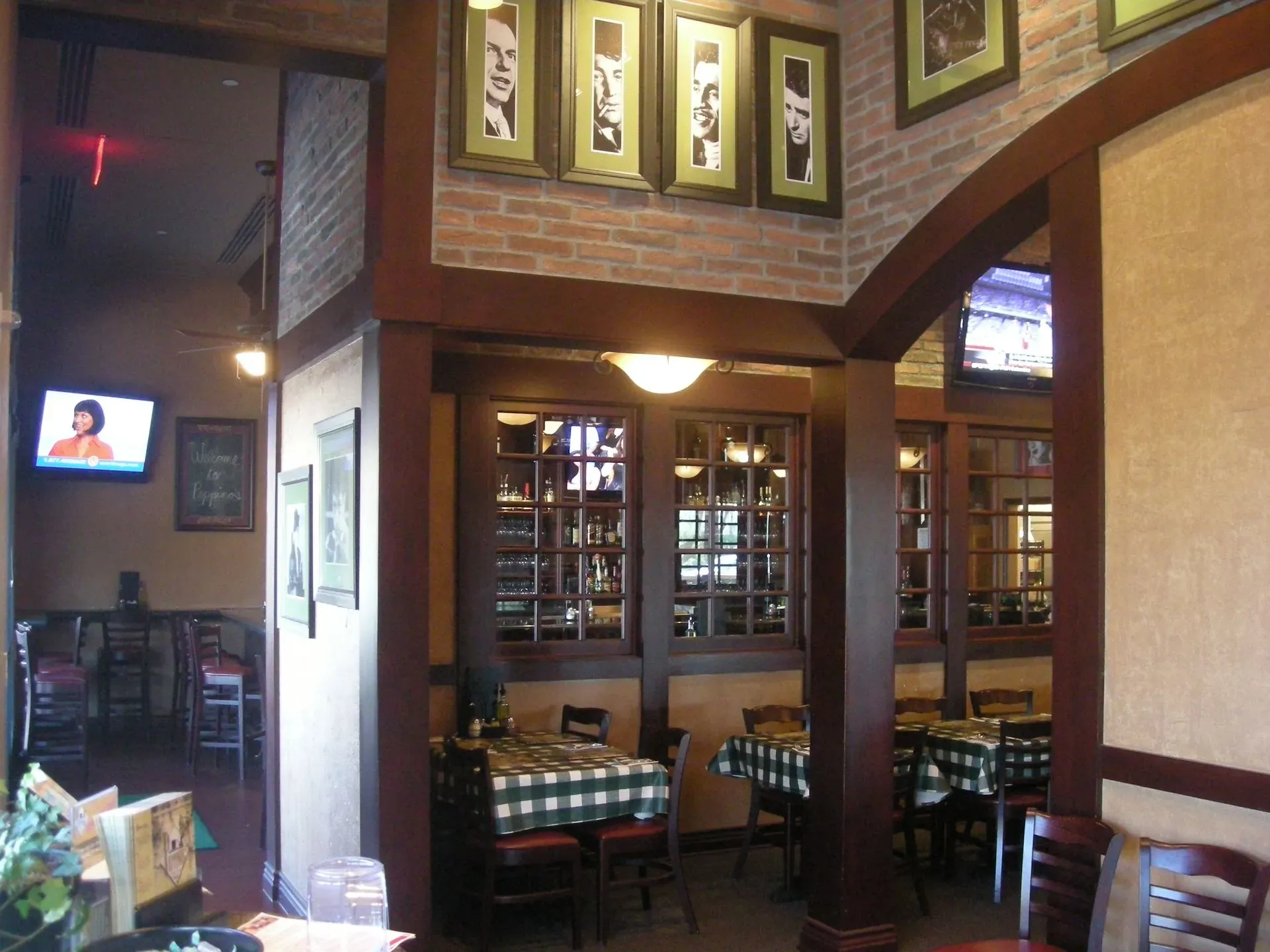 Restaurant interior with brick arches, framed photos, and empty wooden tables by a window