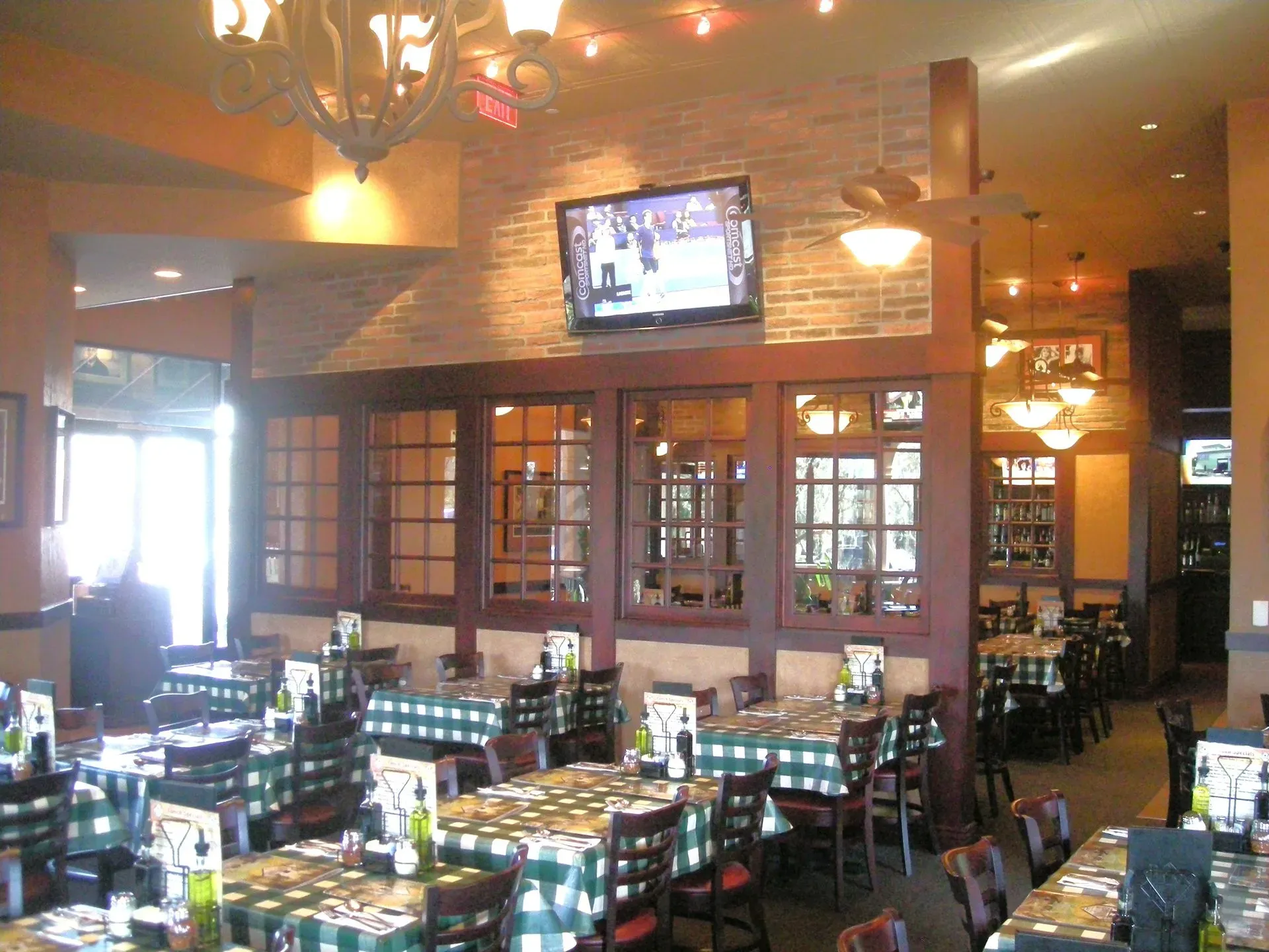 Cozy restaurant dining room with wooden tables, brick walls, warm lighting, and a TV above the bar area