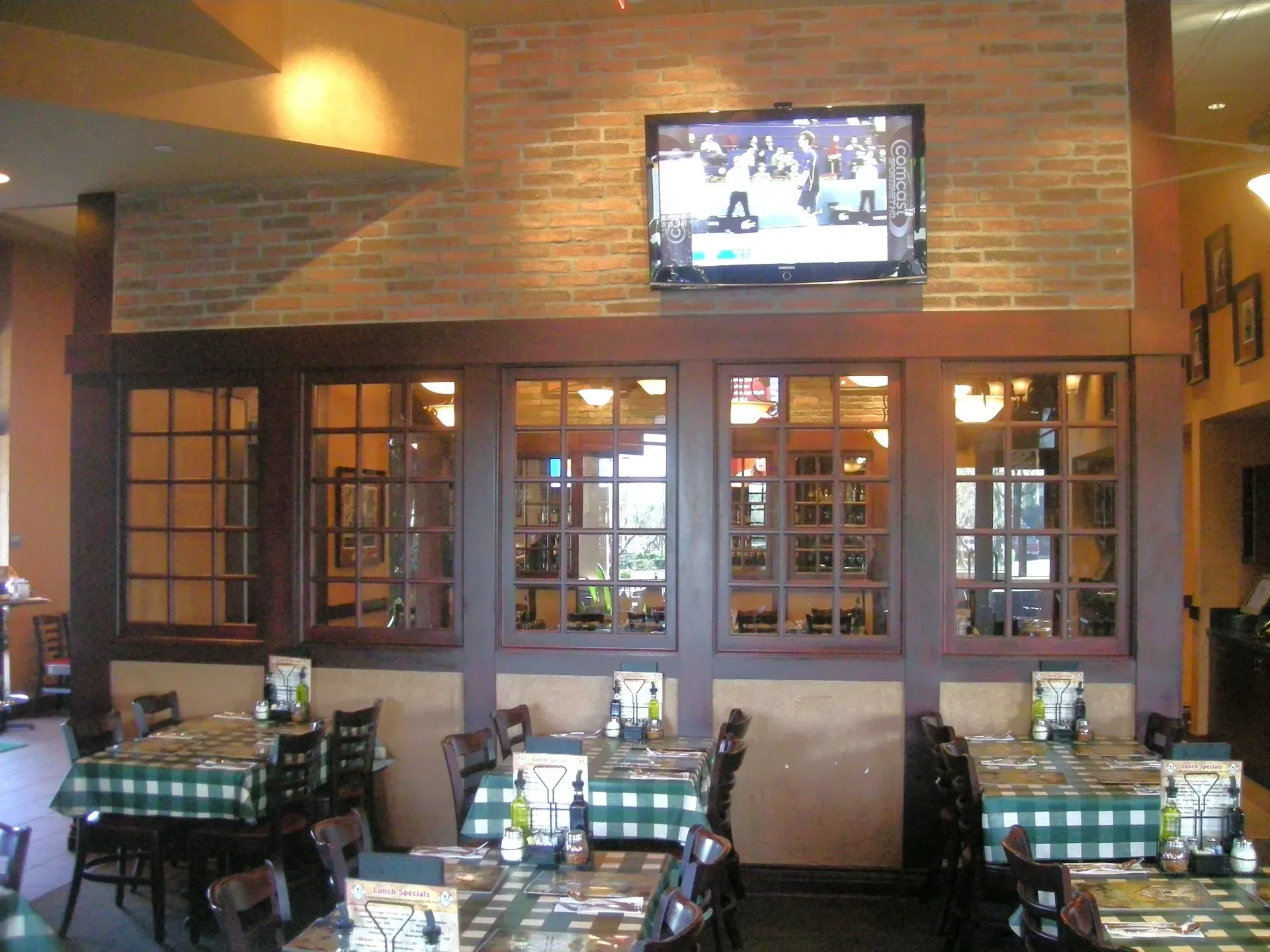 Restaurant dining area with brick walls, dark wood tables, and a TV mounted above the bar