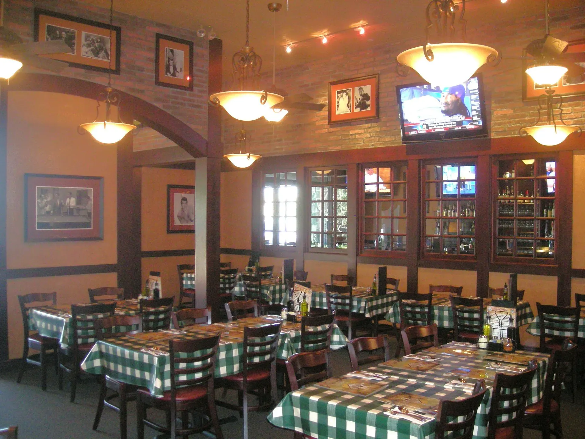 Empty restaurant dining room with checkered tablecloths, hanging lights, and framed wall art