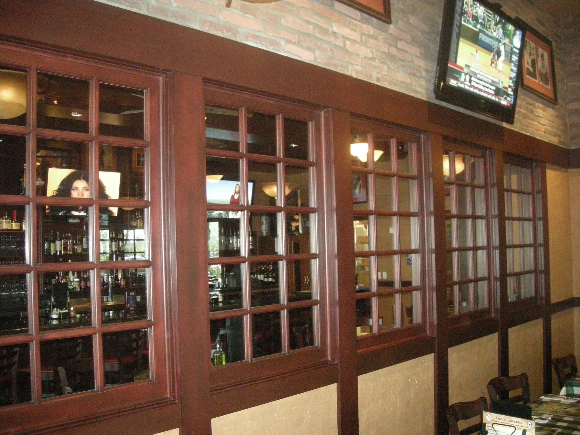 Interior of a cozy restaurant with wood-framed windows, brick walls, and a wall-mounted TV.