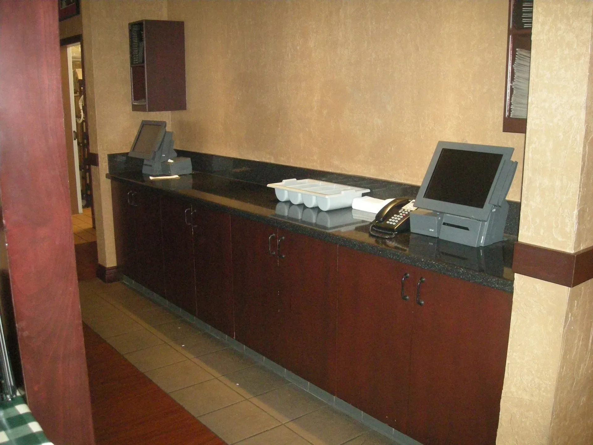 Hotel hallway with a long dark wood counter, computer terminal, and phone against a tan wall.