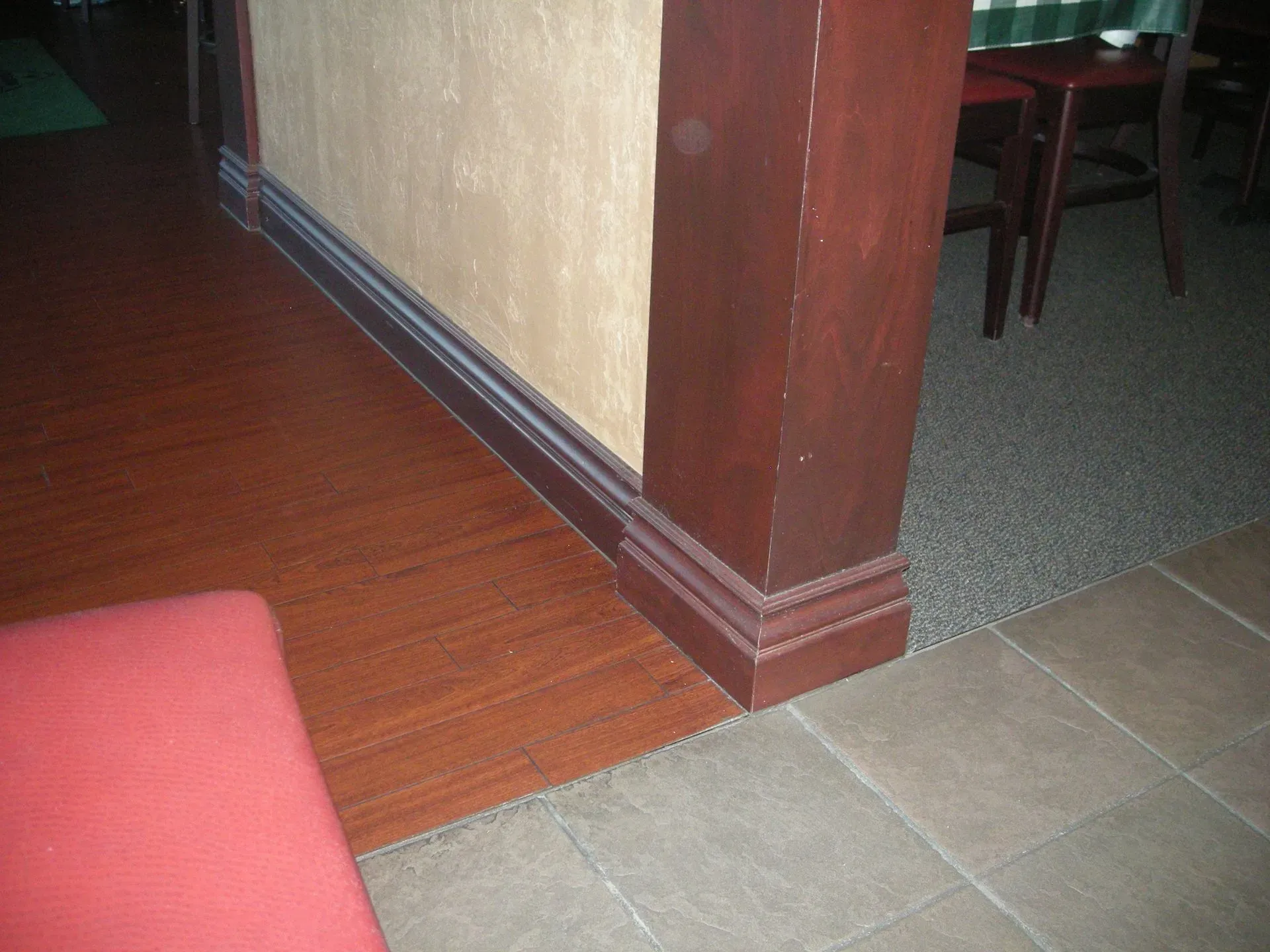 Transition between wood floor, tile, and carpet beside a brown wall corner in an interior room