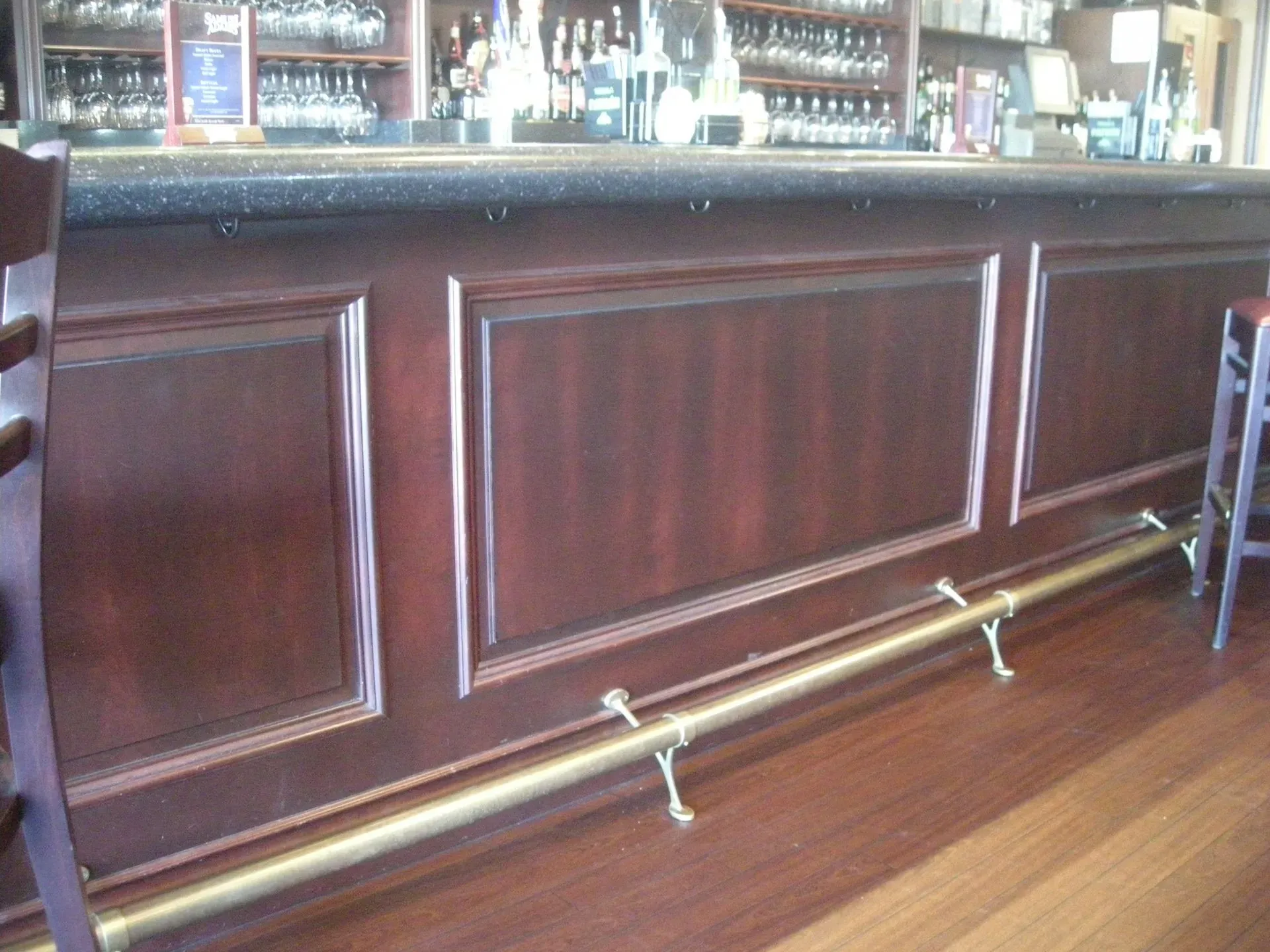 Wooden bar counter with brass foot rail in a pub, with bottles and glasses behind it