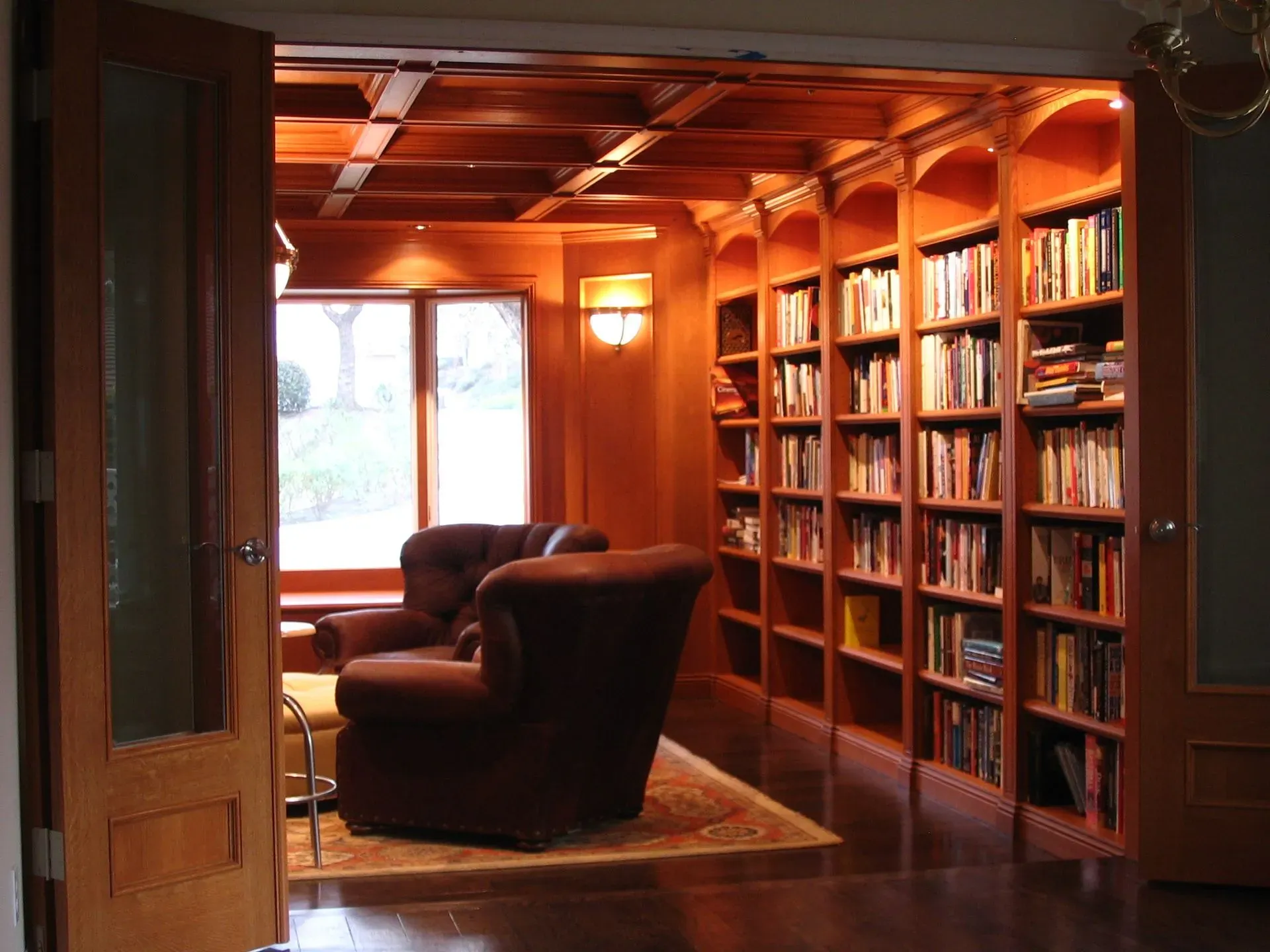 Cozy wood-paneled library with armchairs, bookshelves, and warm lighting beside a window