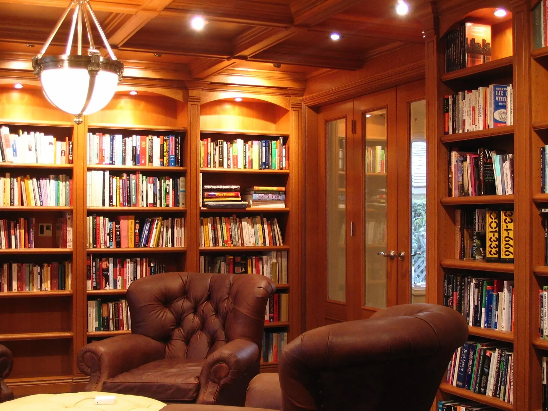 Cozy wood-paneled library with bookshelves, leather chairs, and warm overhead lighting