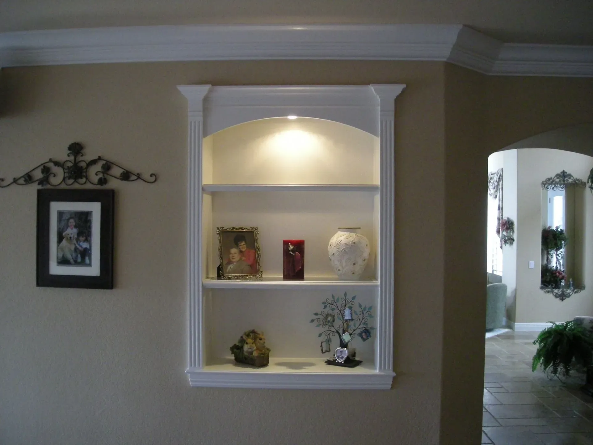Wall niche with built-in shelves, lit top arch, and decorative vases against a beige wall.