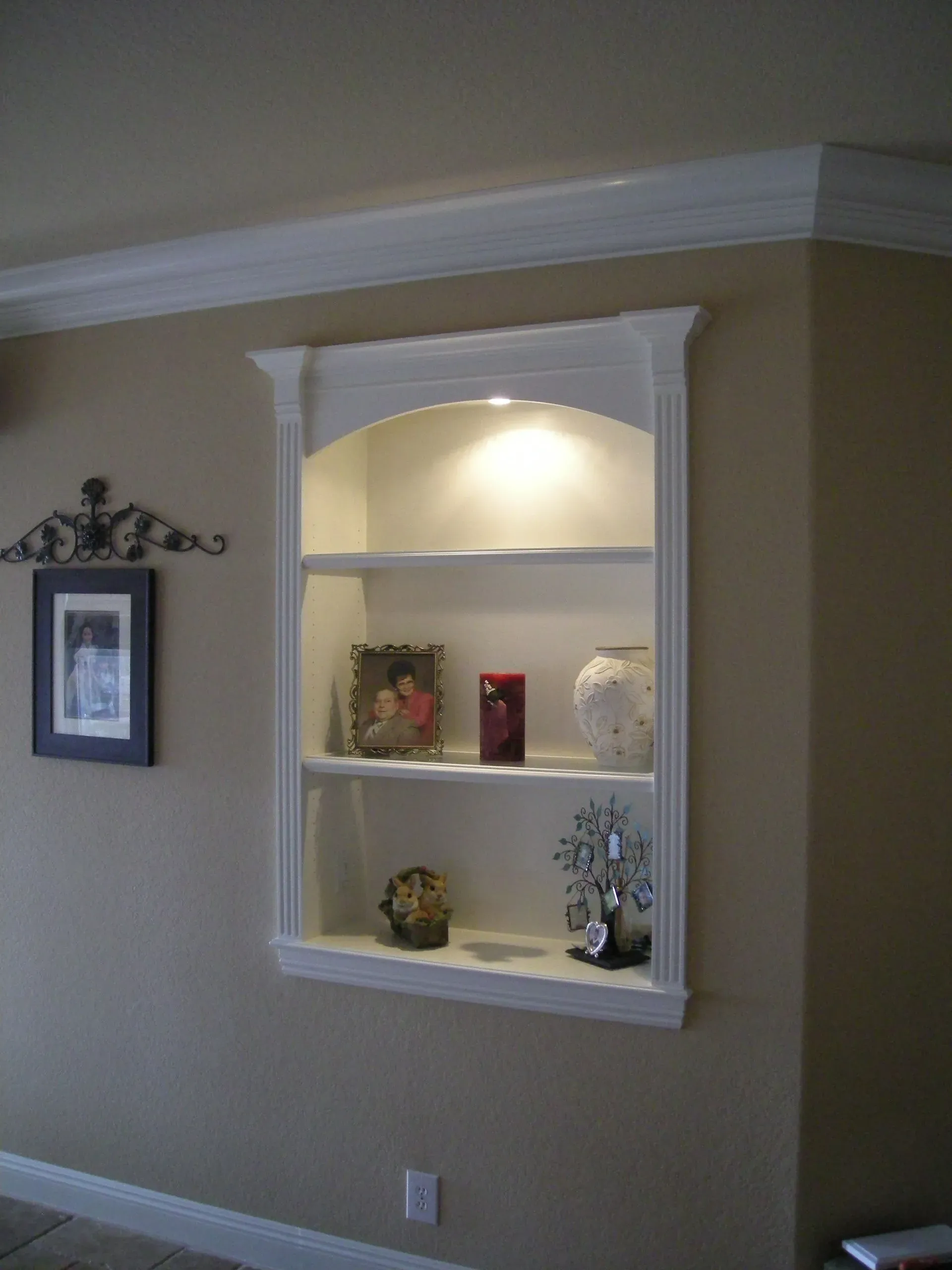 Built-in wall niche with white shelves, lit top alcove, and decorative items in a beige room