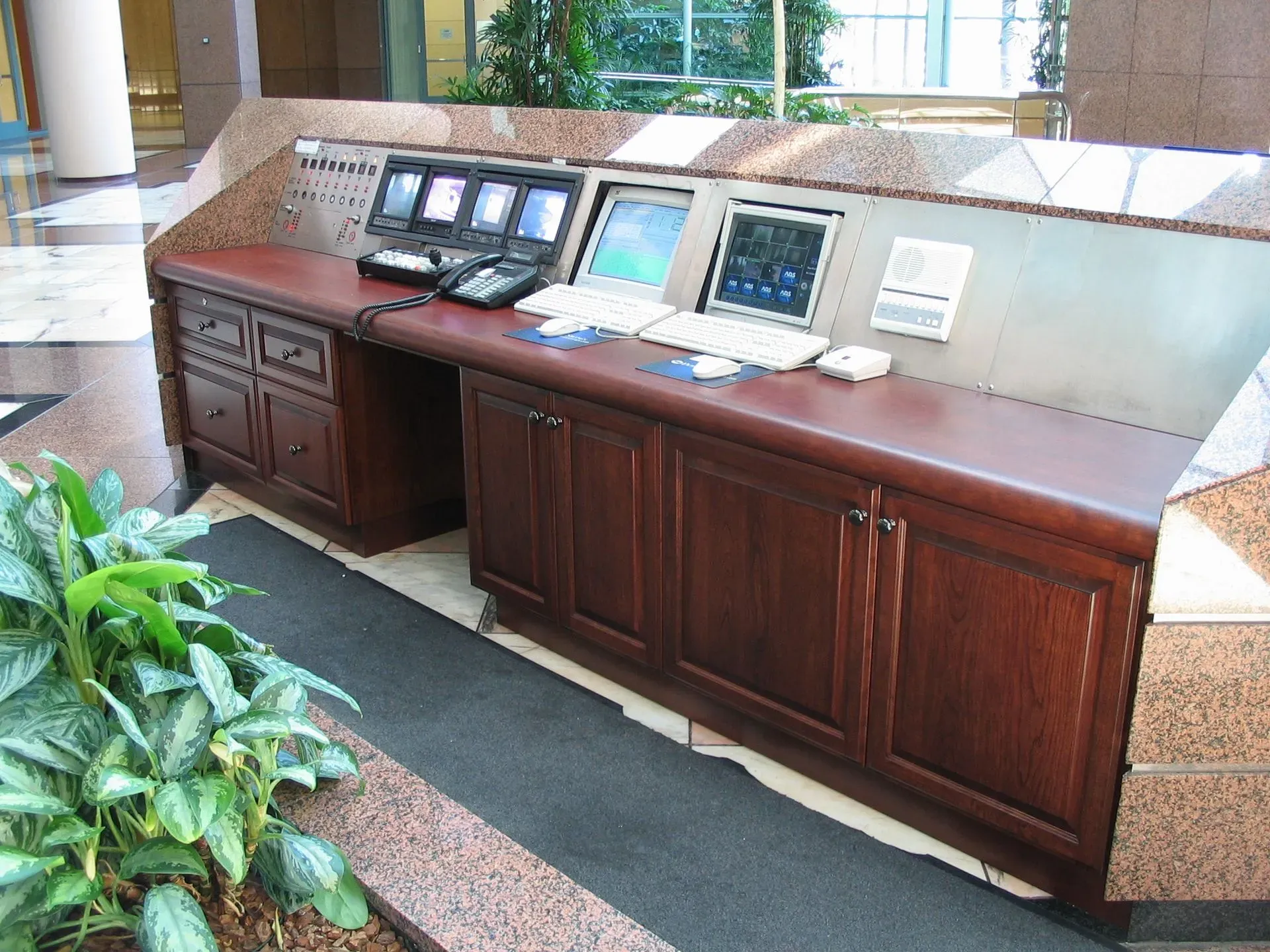 Wooden hotel concierge desk with multiple computer monitors and a marble countertop in a lobby
