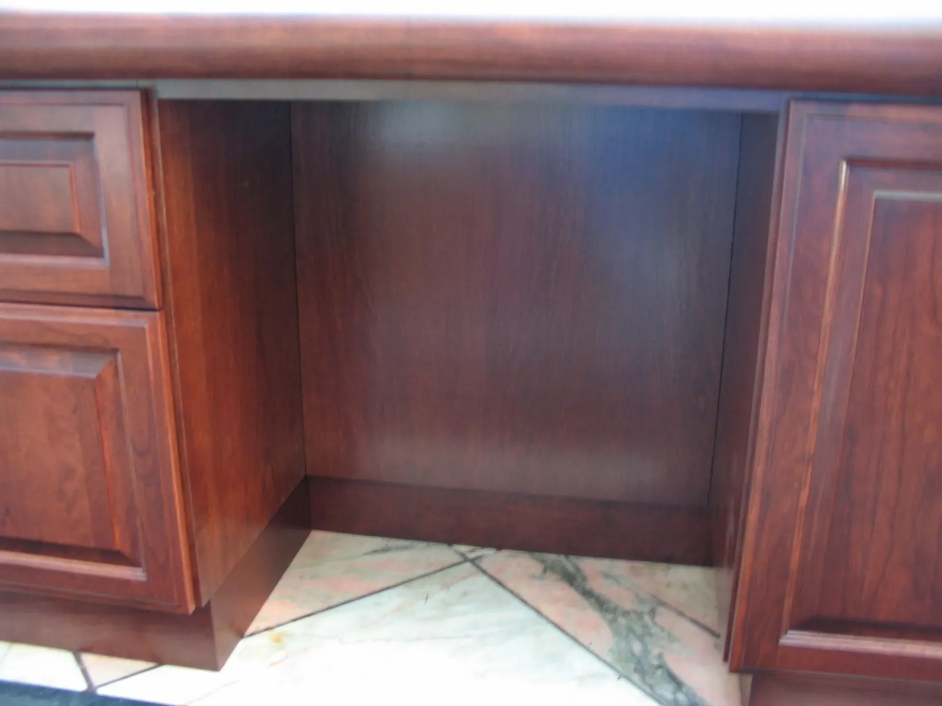 Wooden desk with an open center knee space and drawers on both sides above a marble floor.