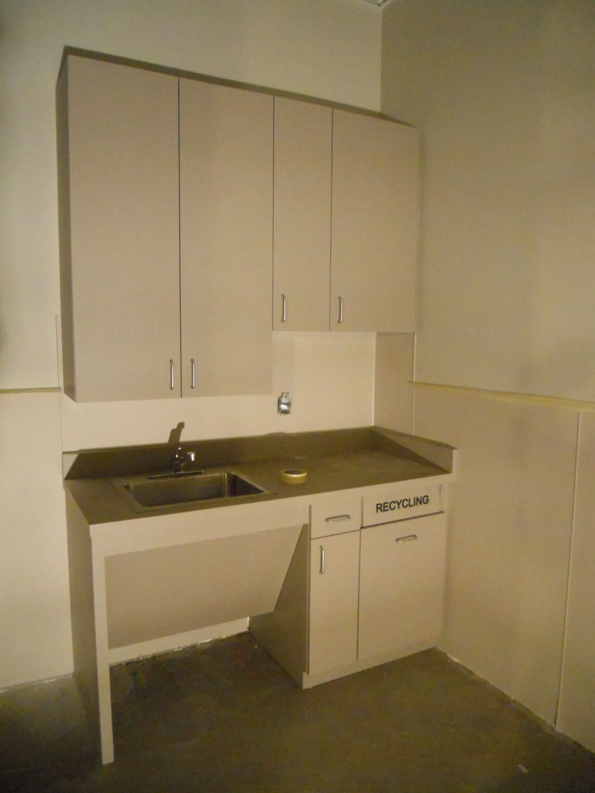 Small kitchenette with beige cabinets, sink, counter, and lower storage in an empty room