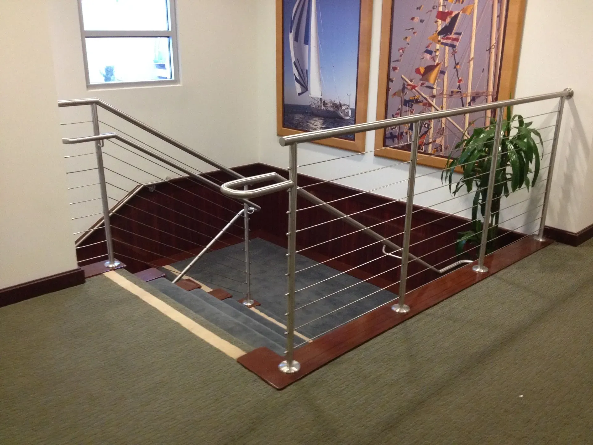 Indoor stair landing with metal railings and framed wall art beside a potted plant.
