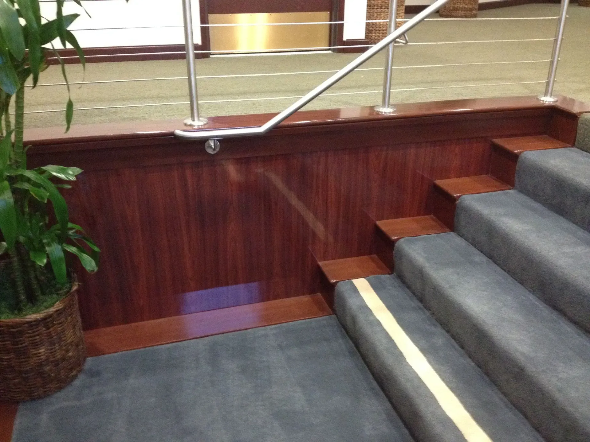 Indoor staircase with gray carpeted steps, wood paneling, and a metal handrail beside a hallway.