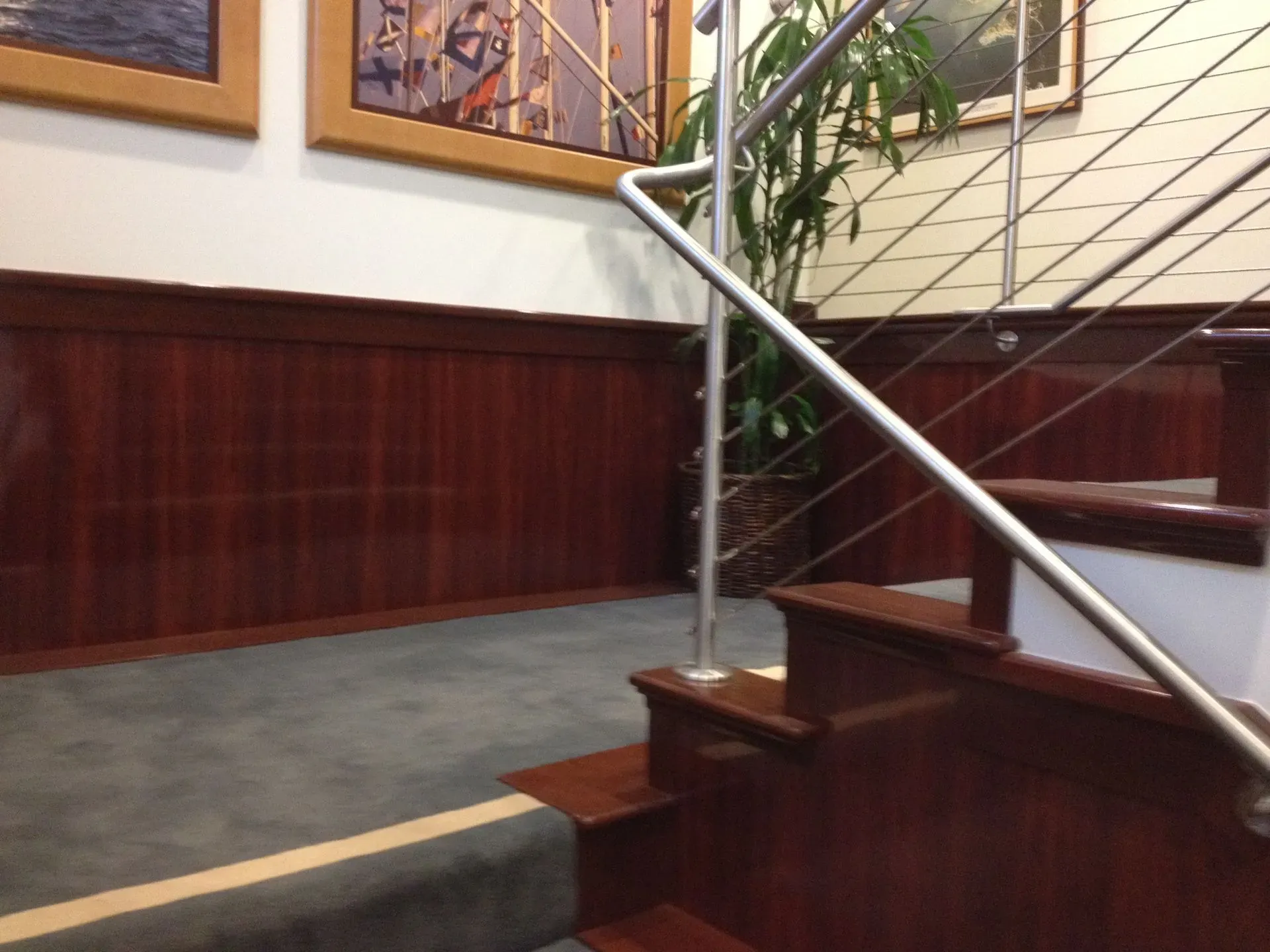 Wood-paneled stairwell with gray carpeted steps and a silver handrail beside framed wall art.