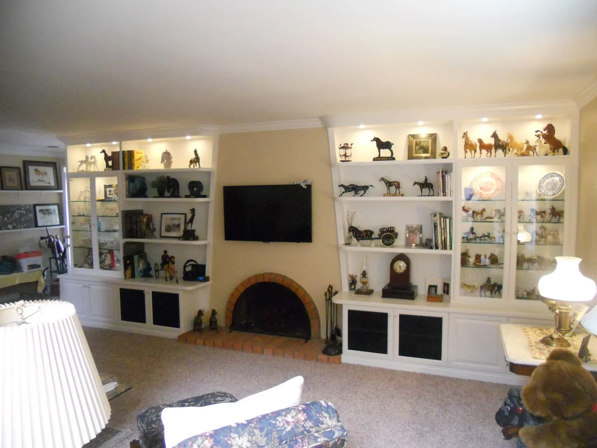 Living room with white built-in shelves, fireplace, TV, and lamps in a warmly lit home interior