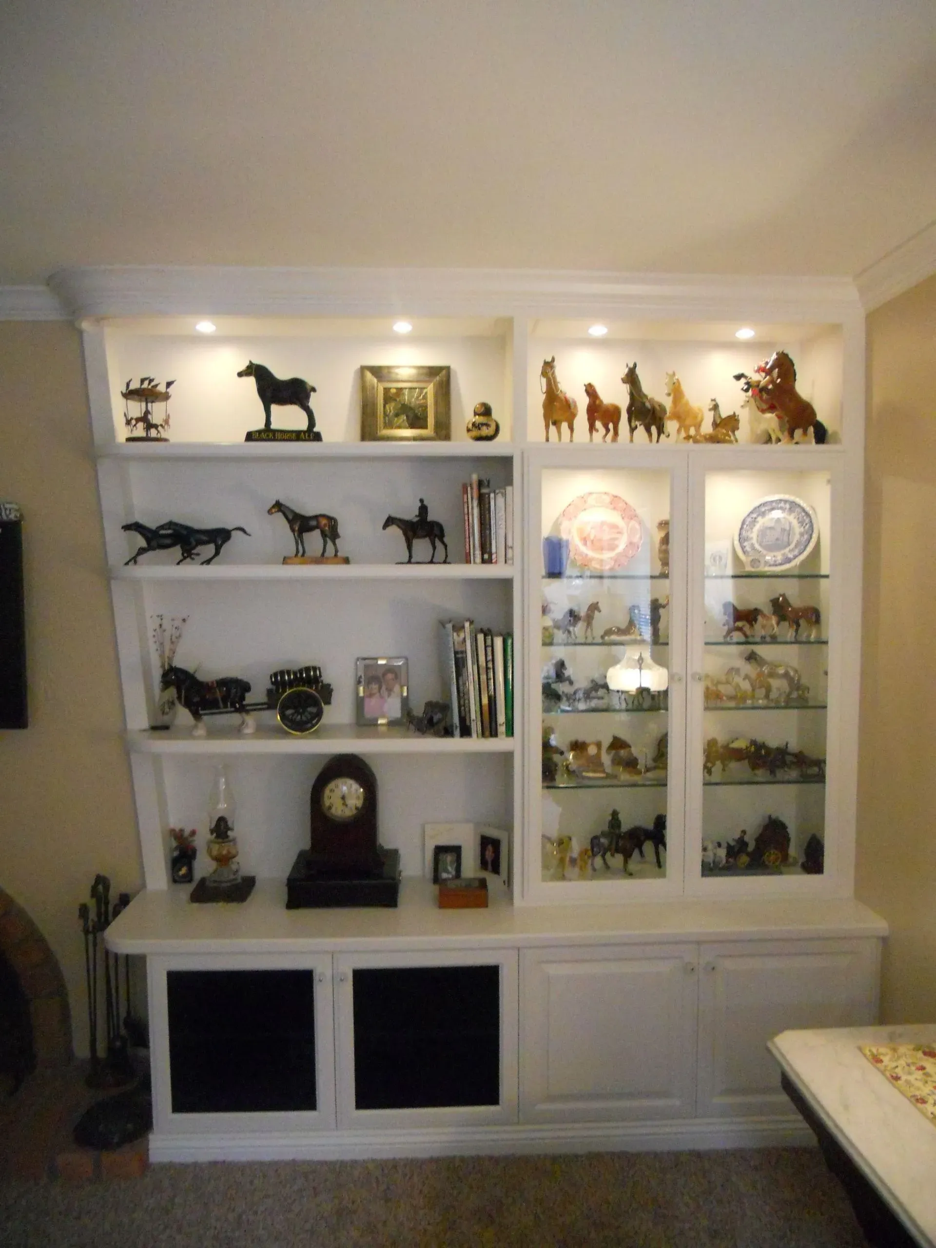 White built-in display cabinet with shelves of figurines, clocks, and glassware in a living room.