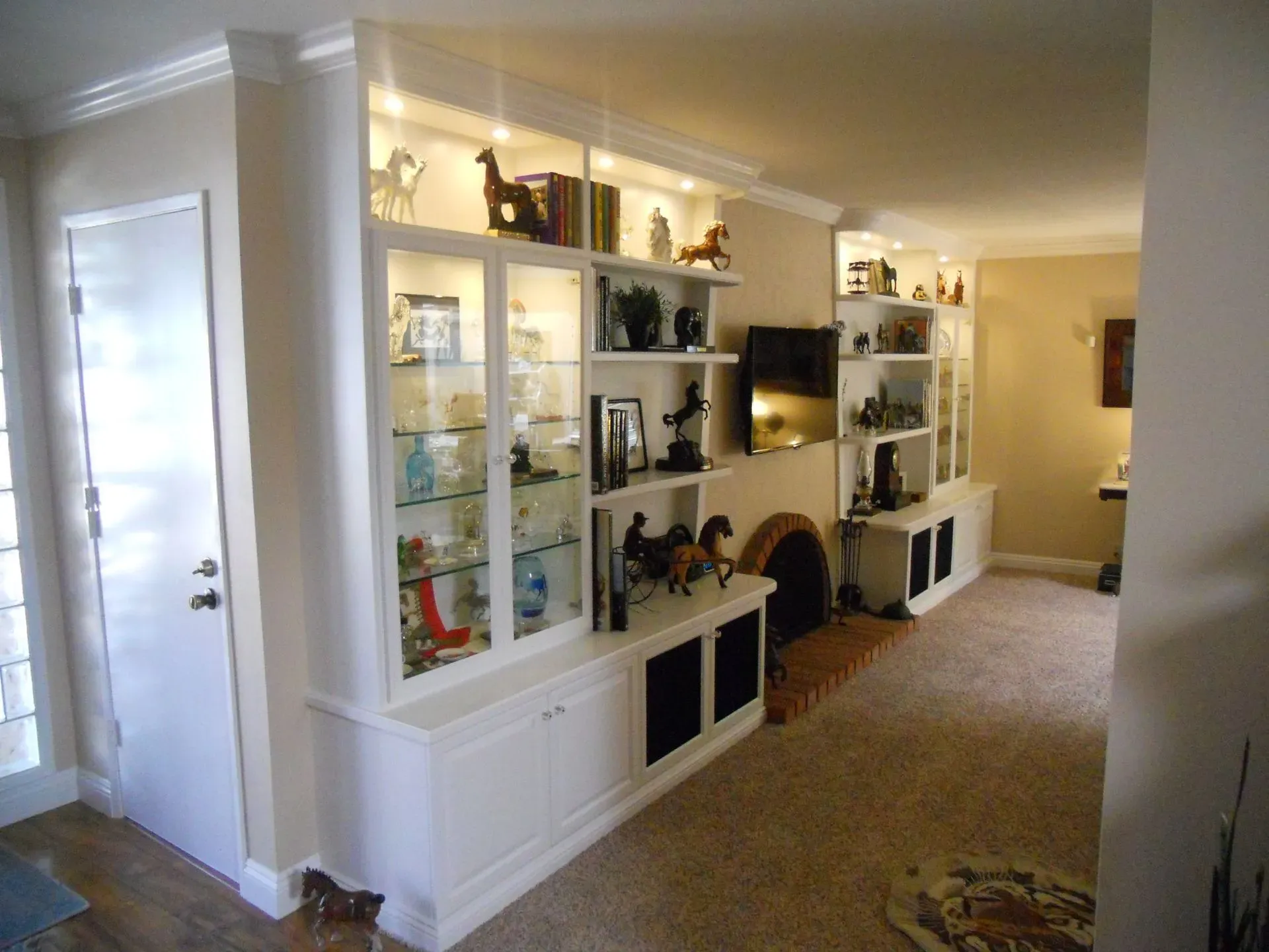Bright hallway with white display cabinets, shelves, and a beige carpet leading to a living room fireplace.