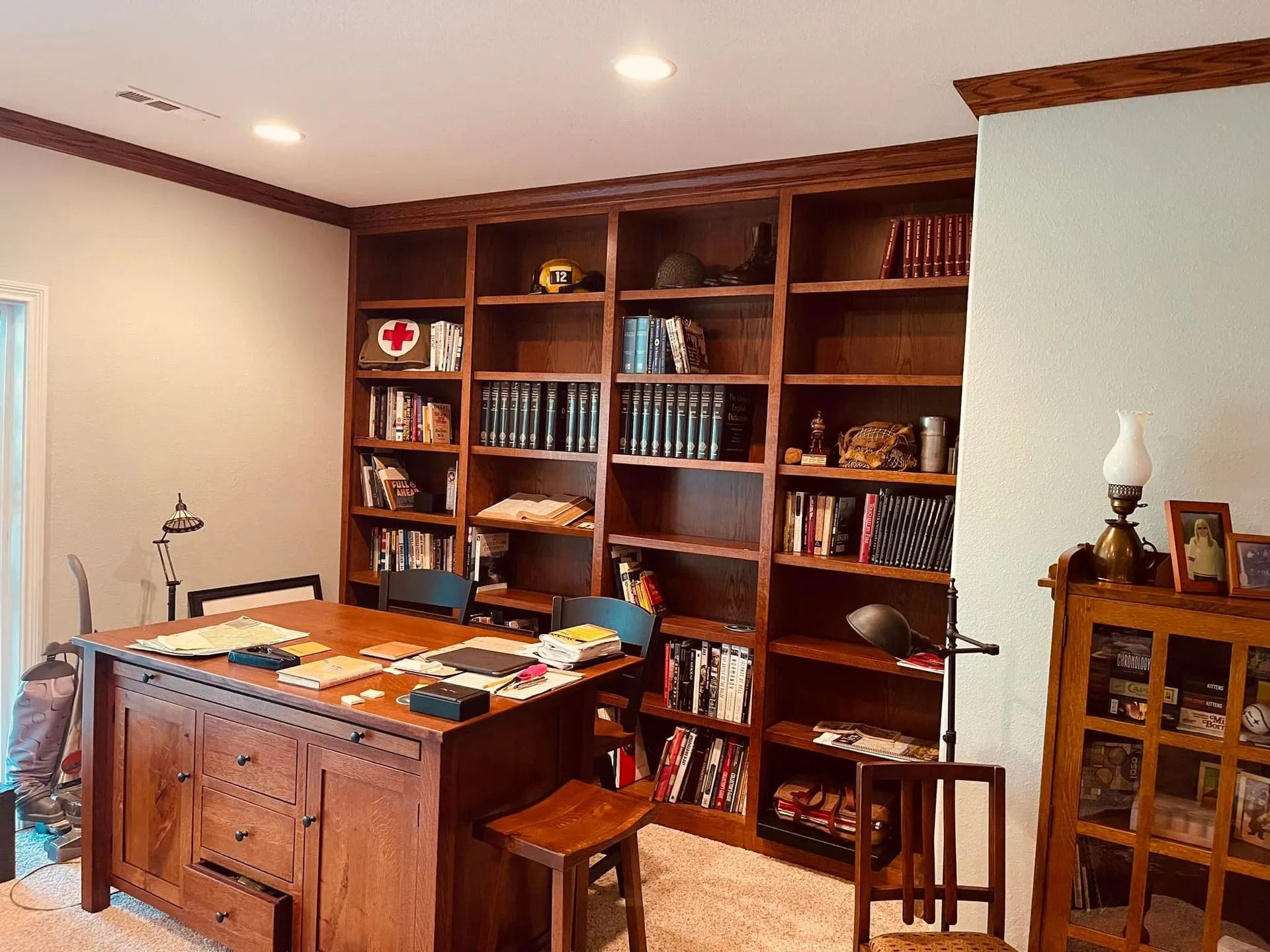 Home office with wooden desk, built-in bookshelves, and a small glass cabinet in a warm, neatly furnished room