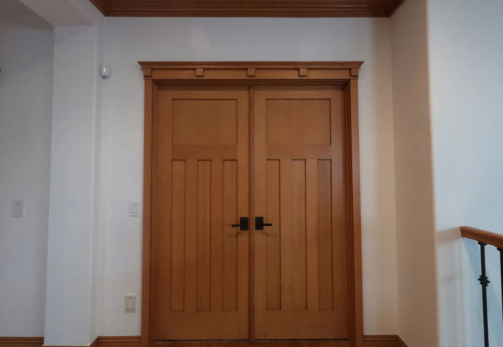 Wooden double doors with black handles in a white hallway