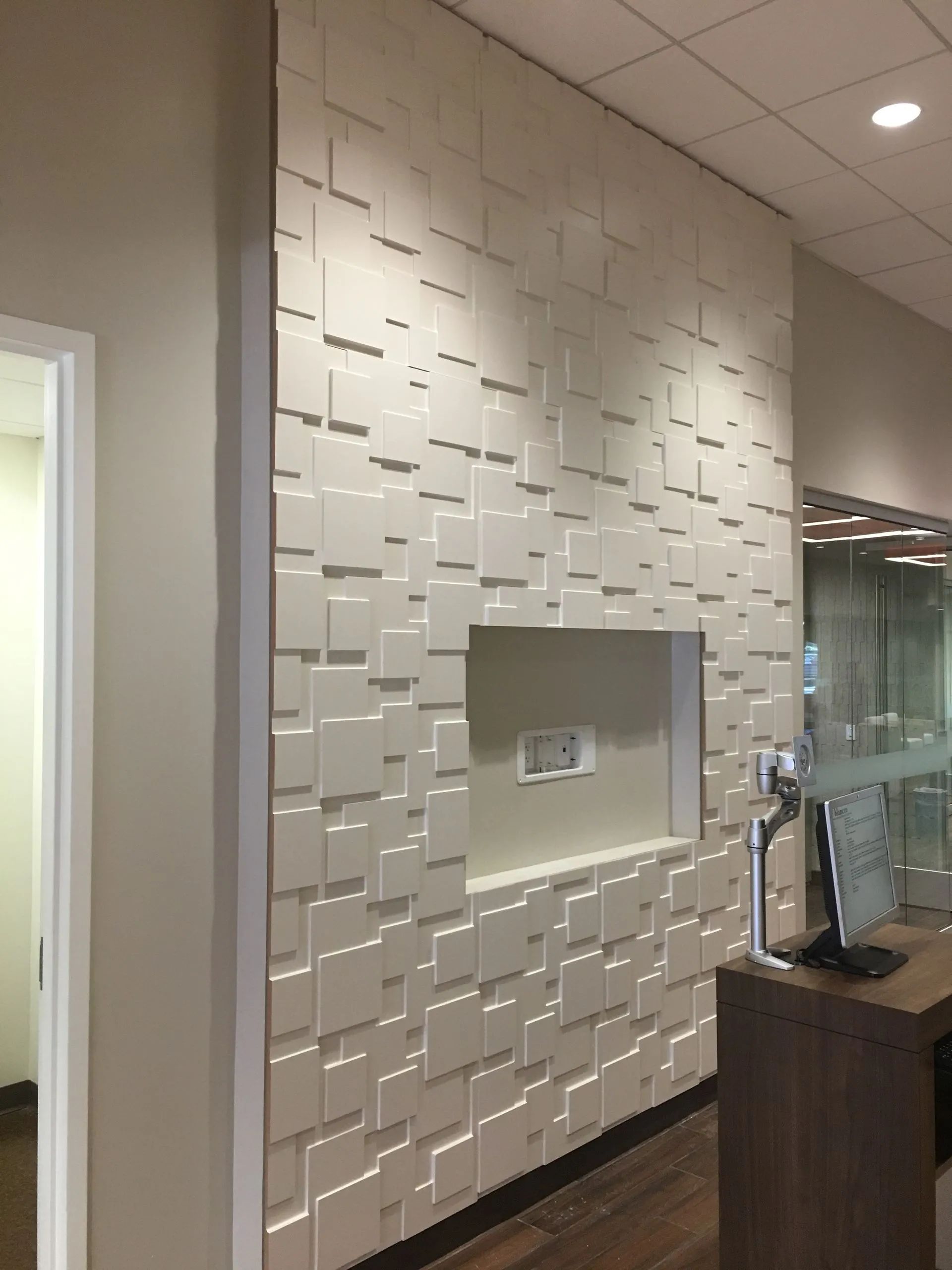 Modern lobby with white textured wall, recessed niche, glass door, and wooden reception desk.