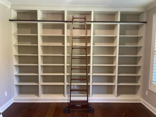 Built-in white bookshelves with a wooden ladder centered on a red library ladder stand