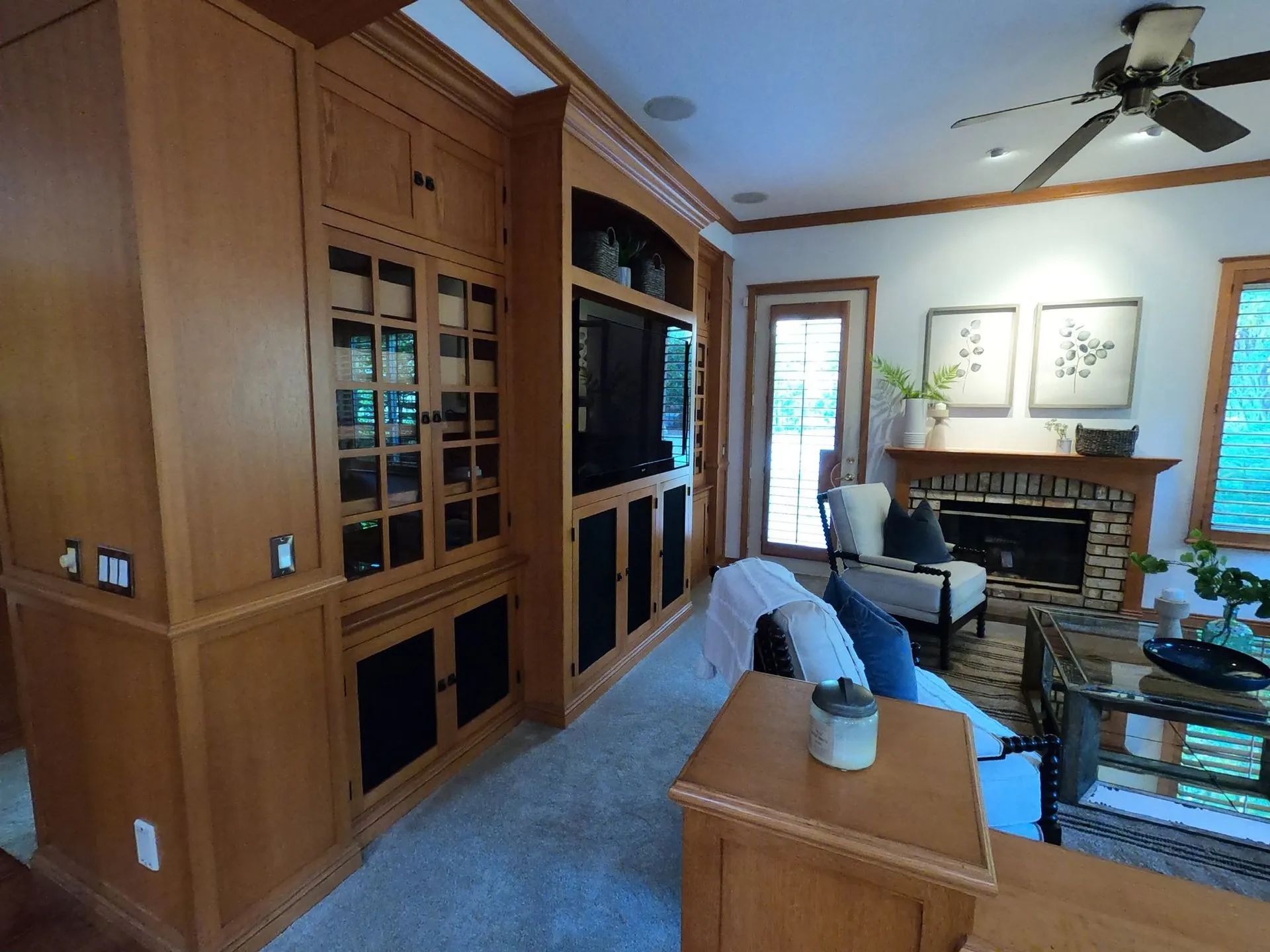 Cozy living room with built-in wooden cabinets, fireplace, gray sofa, and glass coffee tables