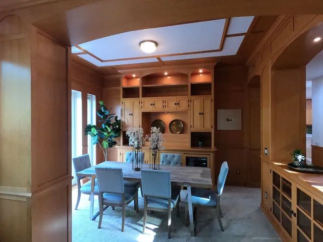 Wood-paneled dining room with a wooden table, chairs, built-in cabinets, and ceiling lights