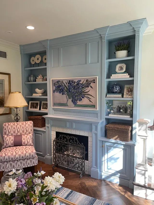 Blue built-in shelves and fireplace in a cozy living room with floral chair and table lamp