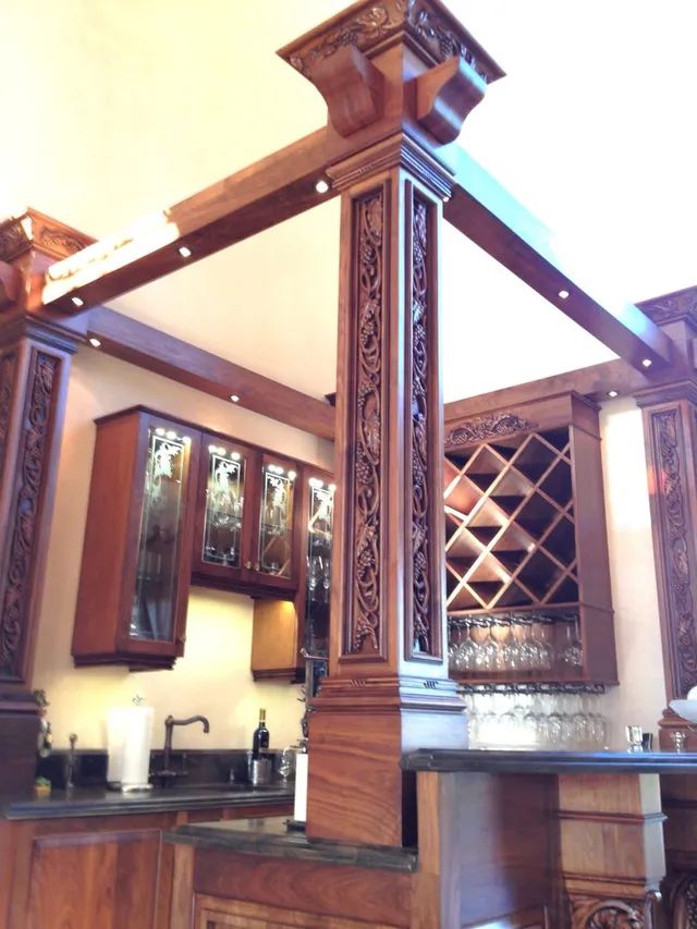 Wooden kitchen with carved columns, dark cabinets, wine rack, and sink beneath a peaked ceiling